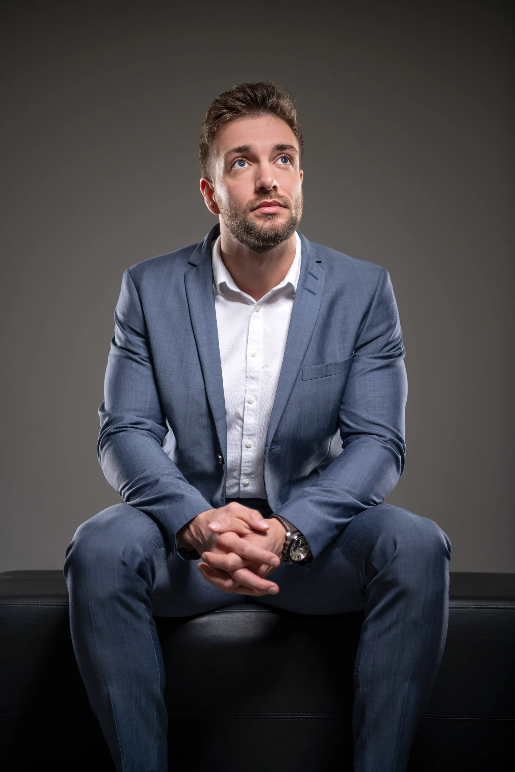 Business Portraits Fotogalerie 022 | Peter Lauritis Photography Mann im blauen Anzug sitzt auf einem Lederhocker und blickt nach oben
