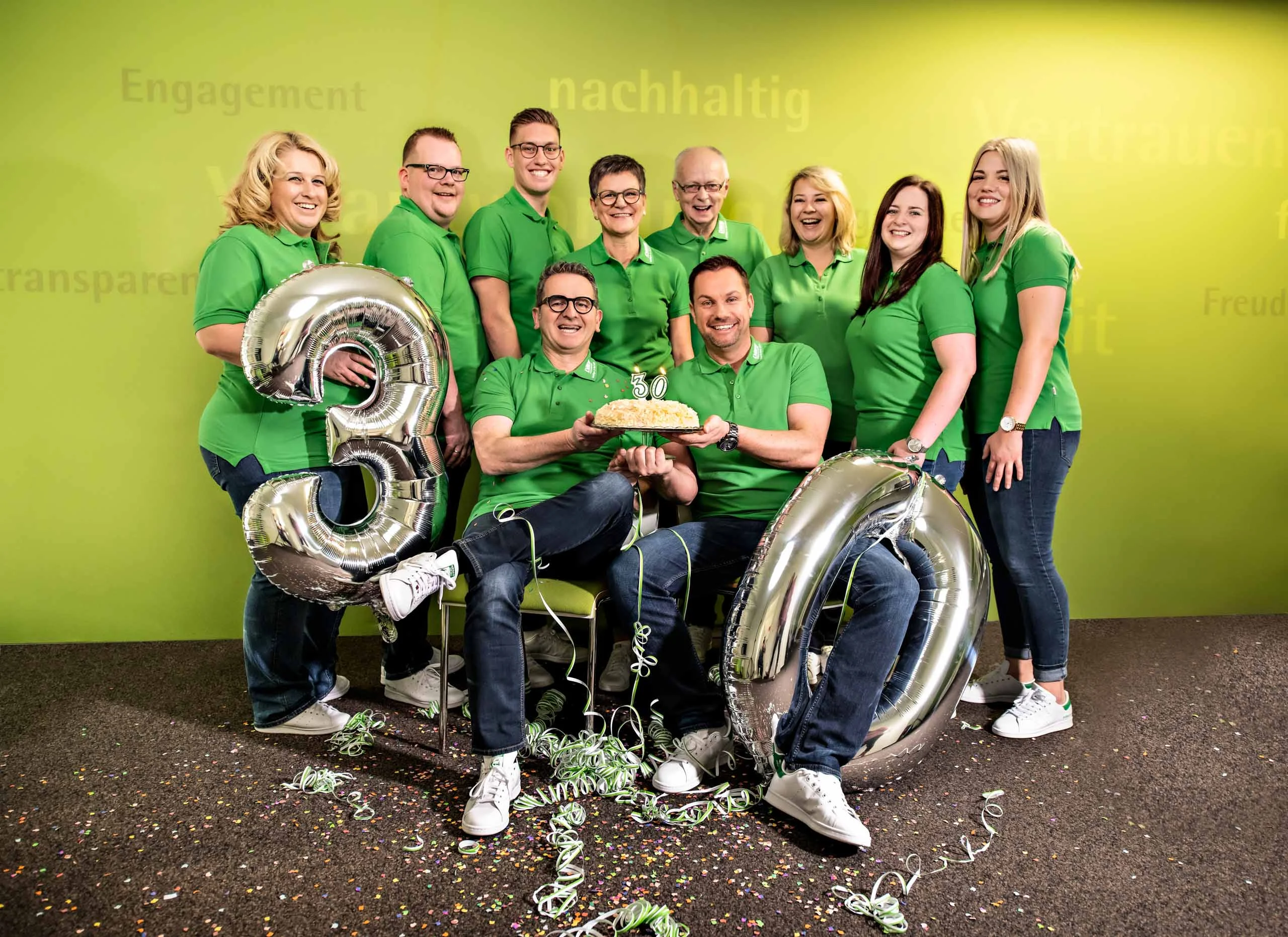 Business Portraits Fotogalerie 032 | Peter Lauritis Photography Team in grünen Poloshirts feiert mit silbernen Ballons „30“ und Torte