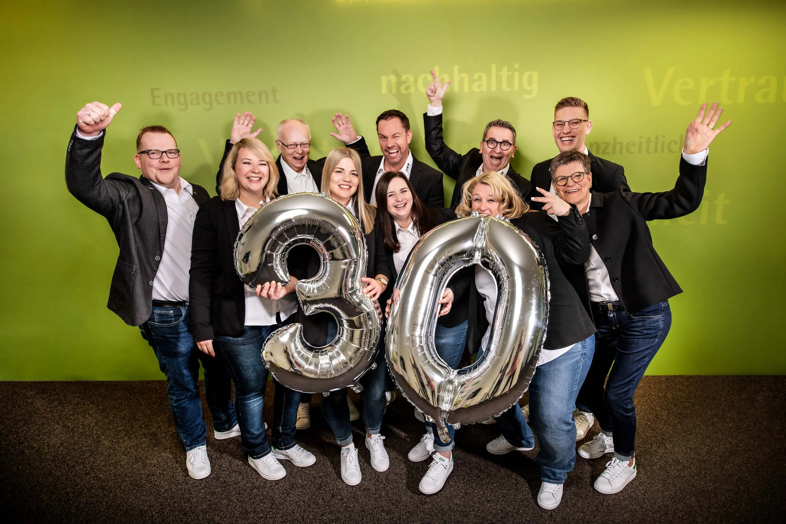 Business Portraits Fotogalerie 034 | Peter Lauritis Photography Team in dunklen Sakkos jubelt mit silbernen Ballons „30“