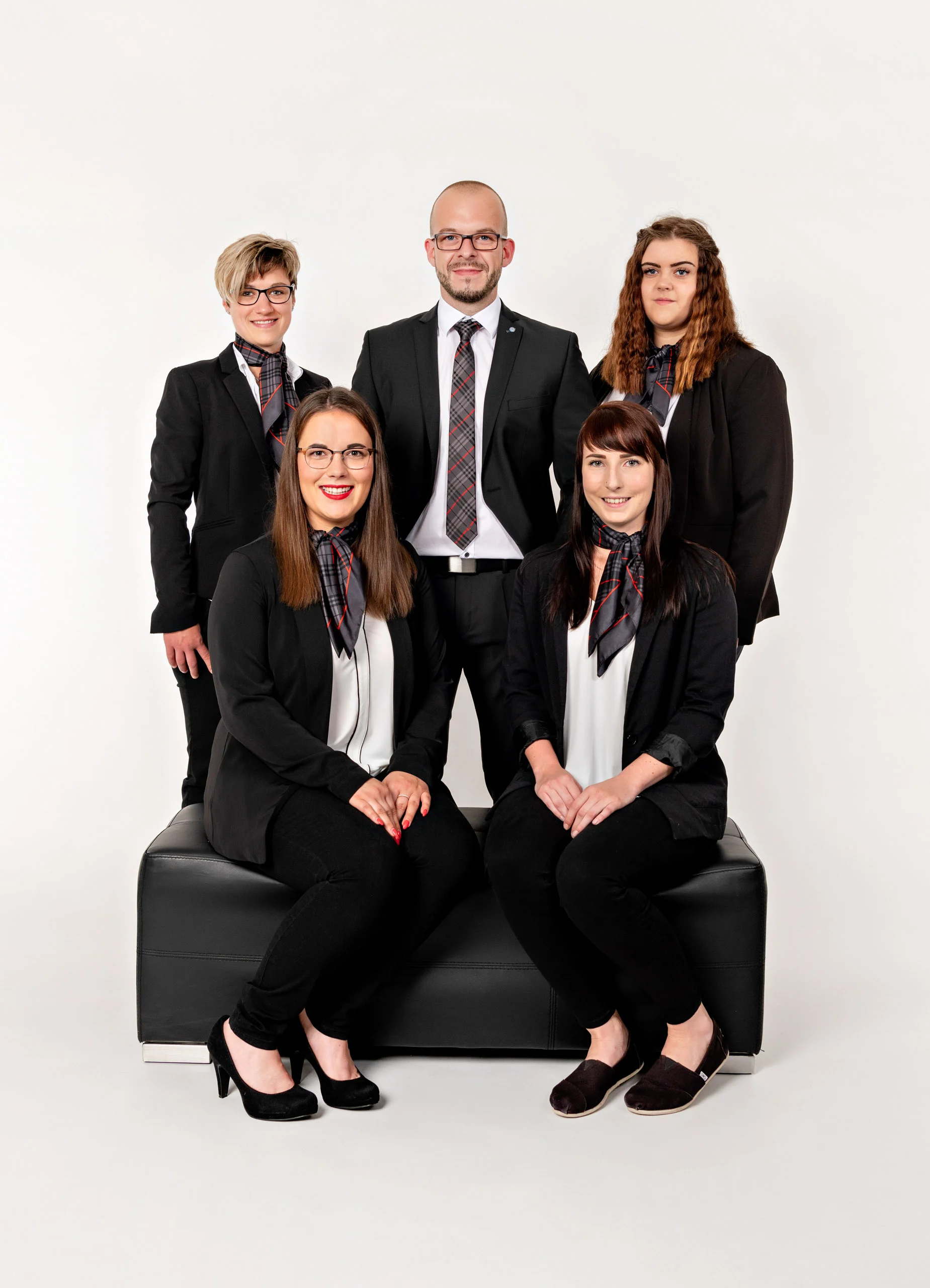 Business Portraits Fotogalerie 043 | Peter Lauritis Photography Team aus fünf Personen in schwarzen Anzügen, zwei sitzen auf einem Lederhocker