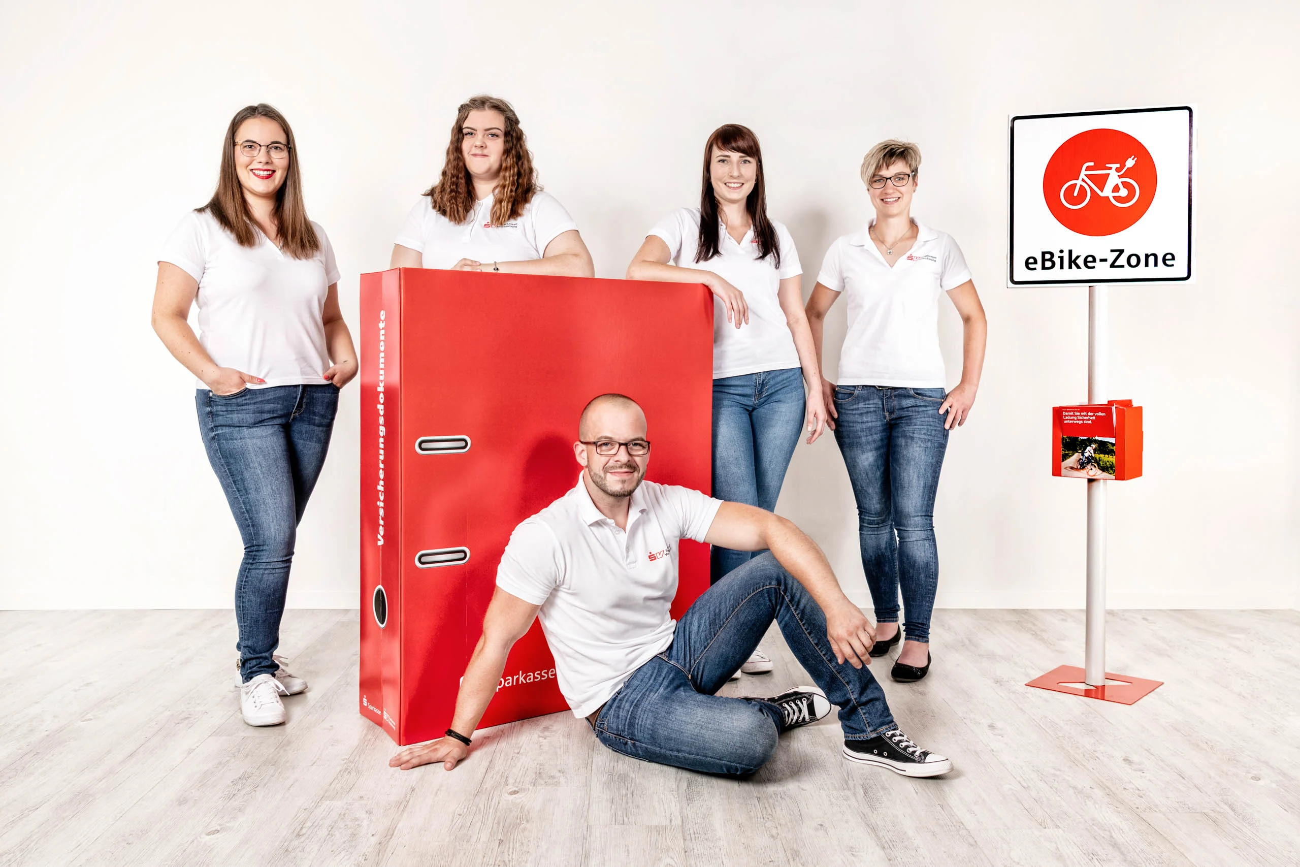 Business Portraits Fotogalerie 046 | Peter Lauritis Photography Team in weißen Shirts, ein Mann sitzt vor einem großen roten Ordner
