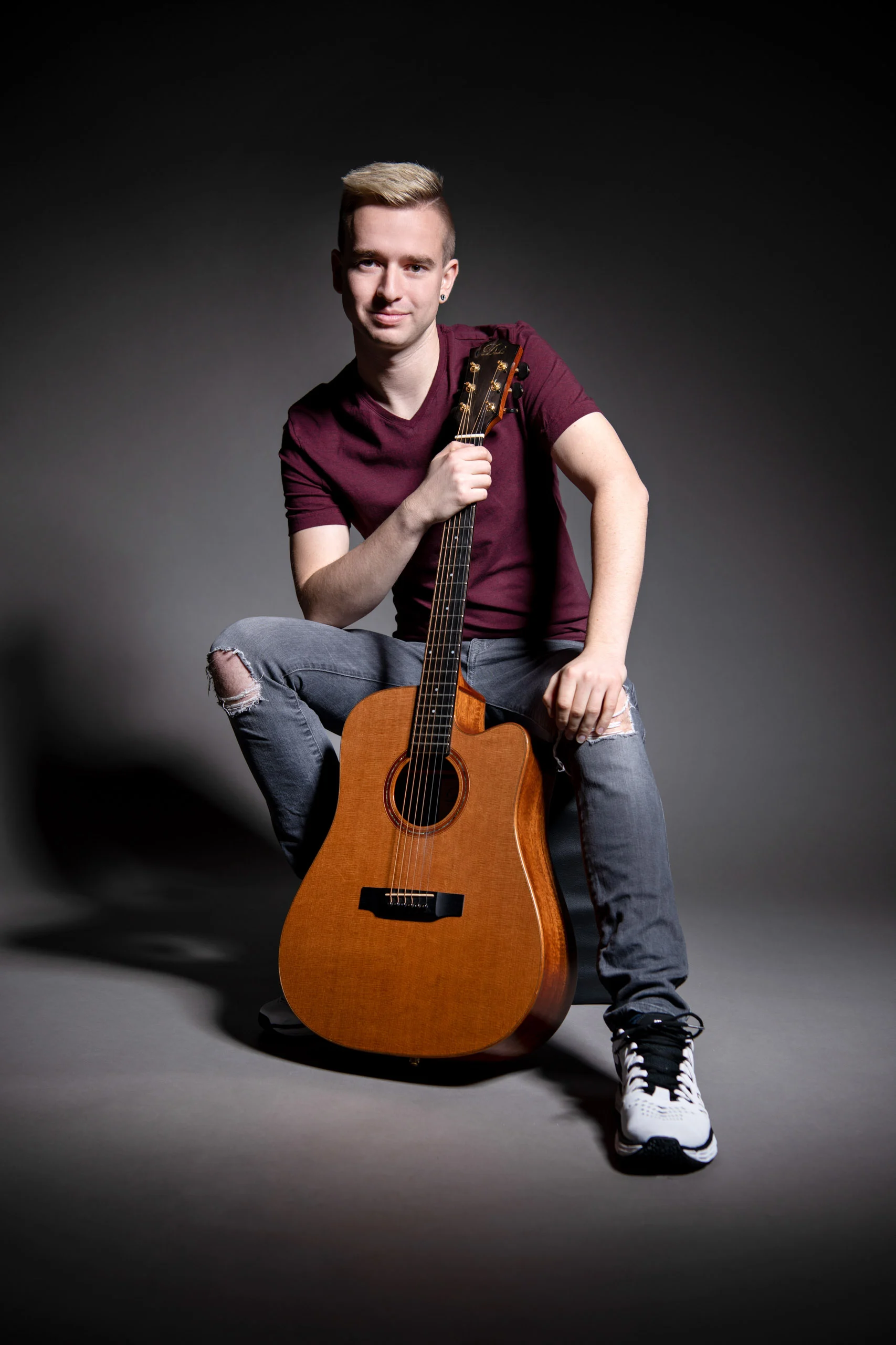 Business Portraits Fotogalerie 048 | Peter Lauritis Photography Junger Mann sitzt mit einer Akustikgitarre vor dunklem Hintergrund
