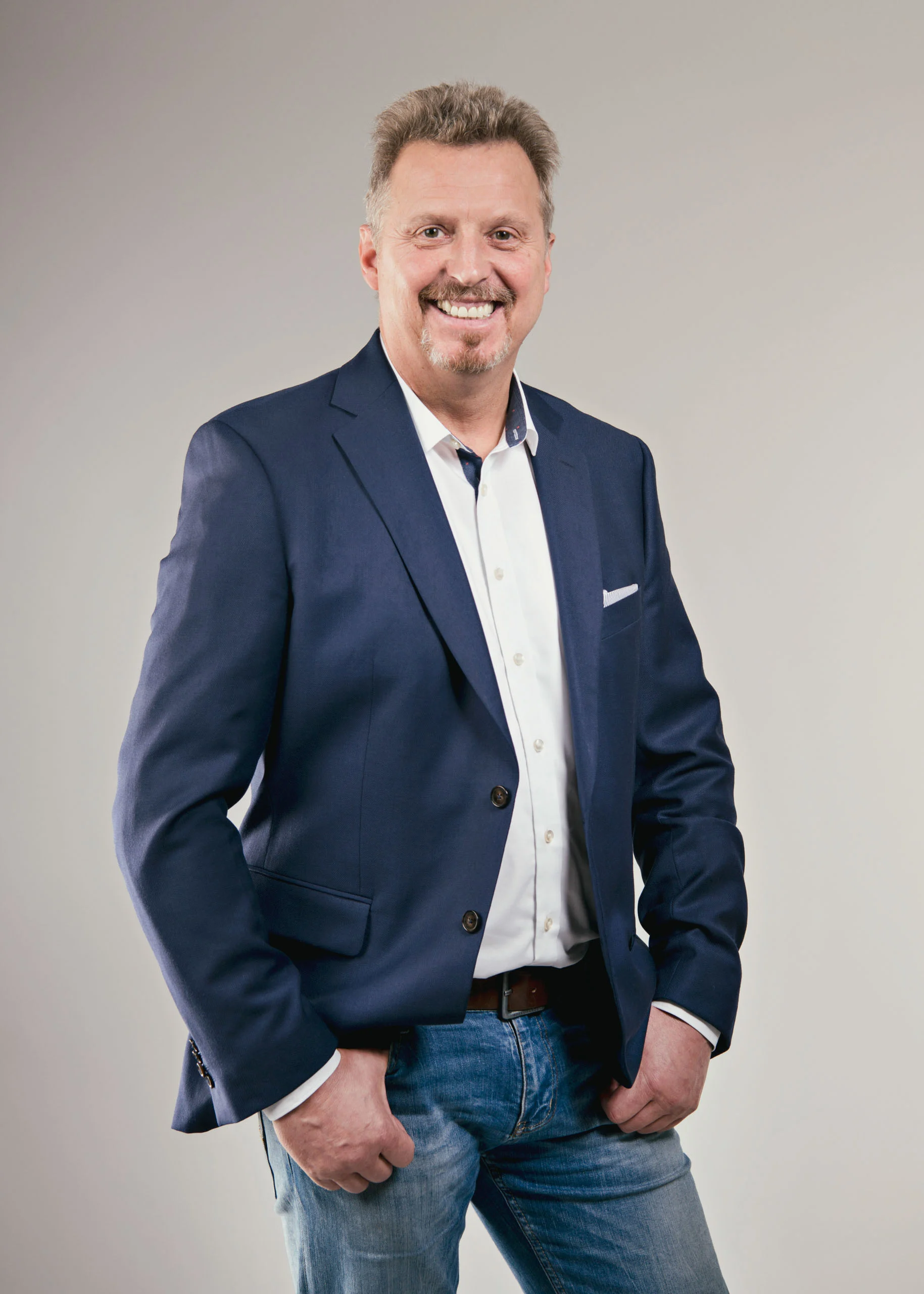 Business Portraits Fotogalerie 057 | Peter Lauritis Photography Lächelnder Mann im dunkelblauen Sakko mit Jeans und Händen in den Taschen
