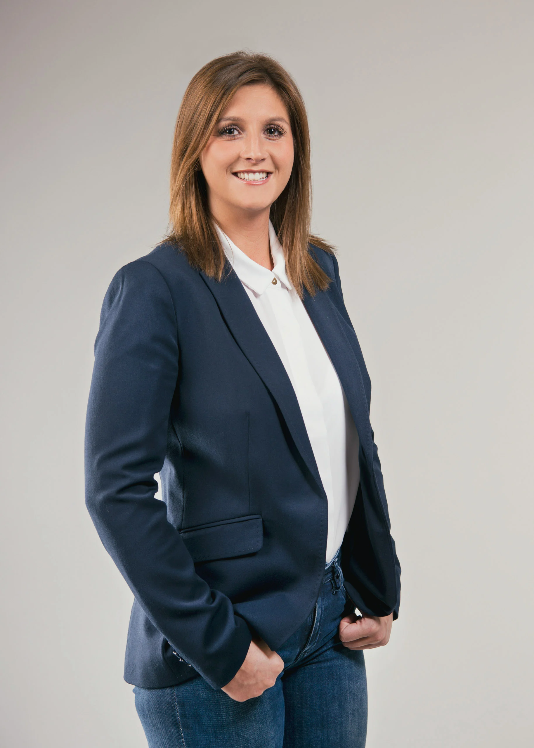 Business Portraits Fotogalerie 059 | Peter Lauritis Photography Frau im dunkelblauen Blazer mit Jeans lächelt vor grauem Hintergrund