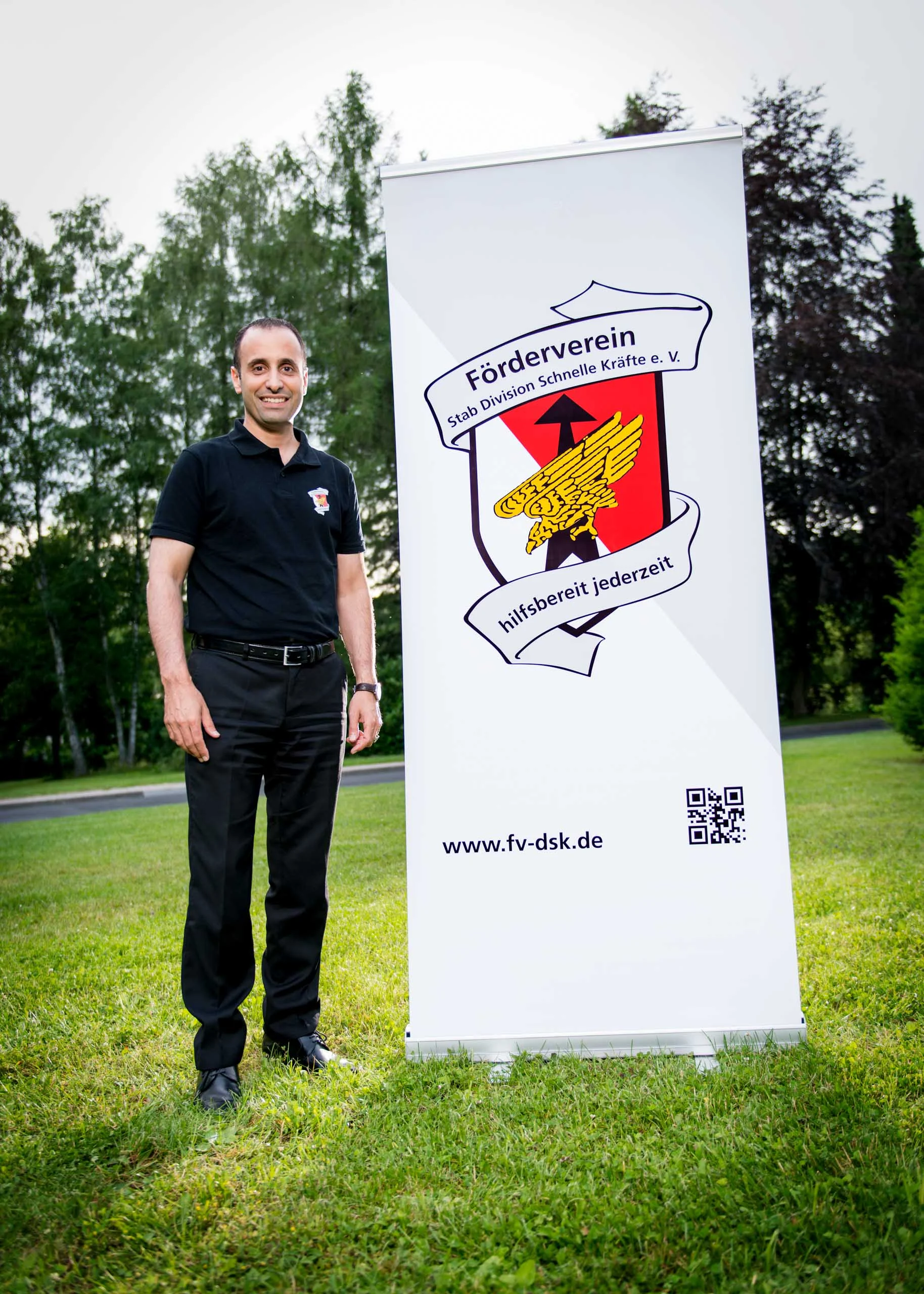Business Portraits Fotogalerie 079 | Peter Lauritis Photography Mann in Schwarz steht neben einem Banner eines Fördervereins auf einer Wiese
