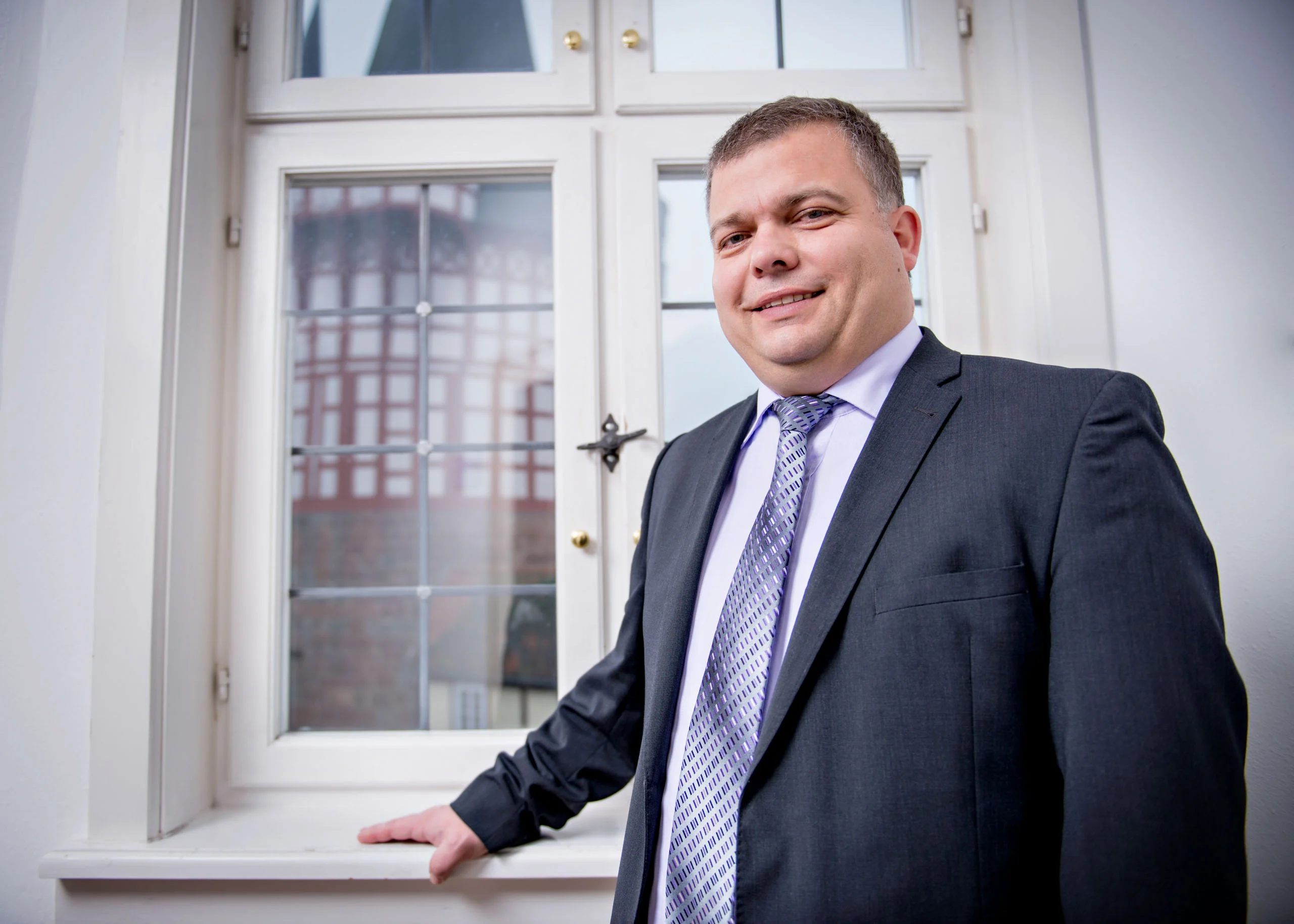 Business Portraits Fotogalerie 081 | Peter Lauritis Photography Mann im Anzug steht lächelnd an einem Fenster