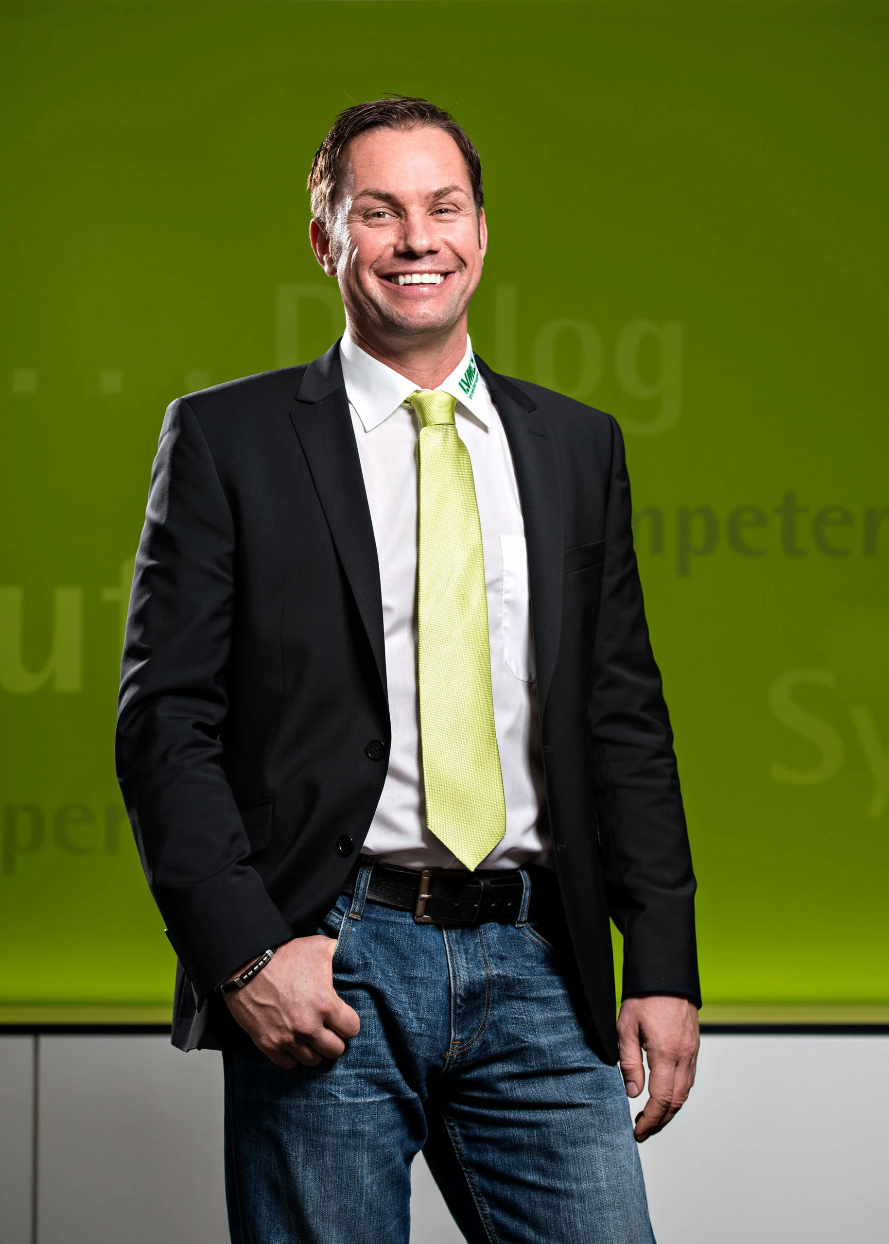 Business Portraits Fotogalerie 088 | Peter Lauritis Photography Mann mit grüner Krawatte und Händen in den Taschen vor grüner Wand
