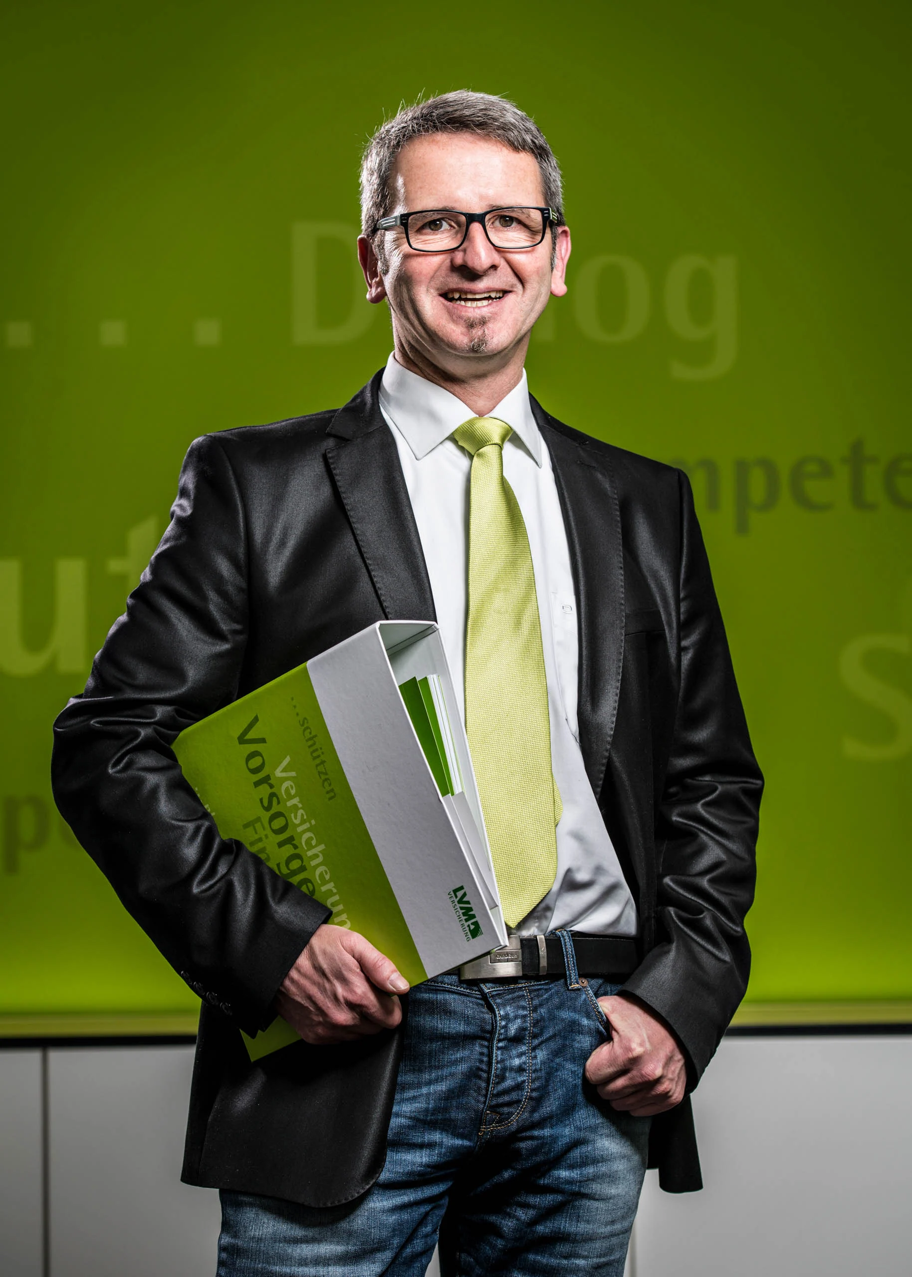 Business Portraits Fotogalerie 089 | Peter Lauritis Photography Mann mit Brille und Lederjacke hält eine Mappe vor grüner Wand