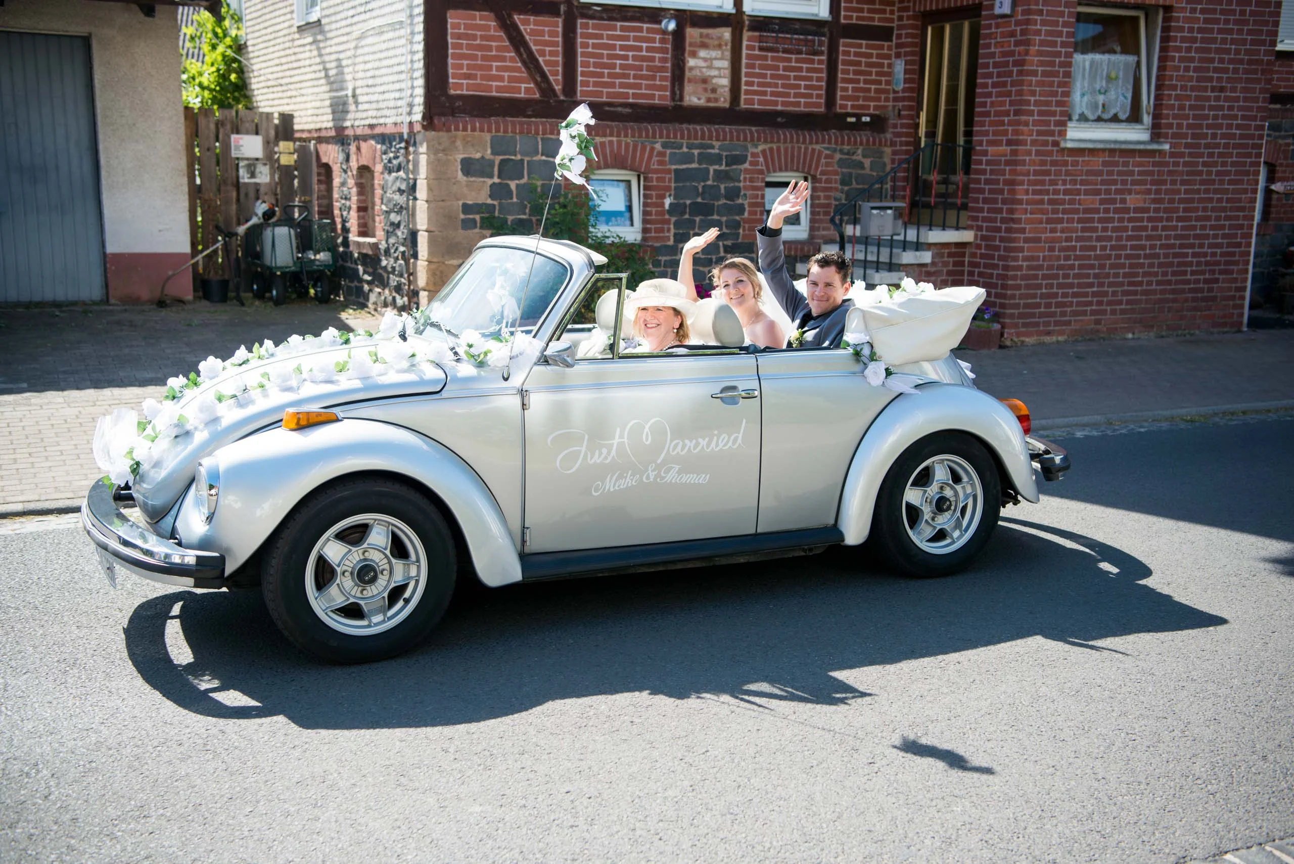 Hochzeitsfeier Fotogalerie 007 | Peter Lauritis Photography Brautpaar winkt aus einem geschmückten VW-Käfer-Cabrio