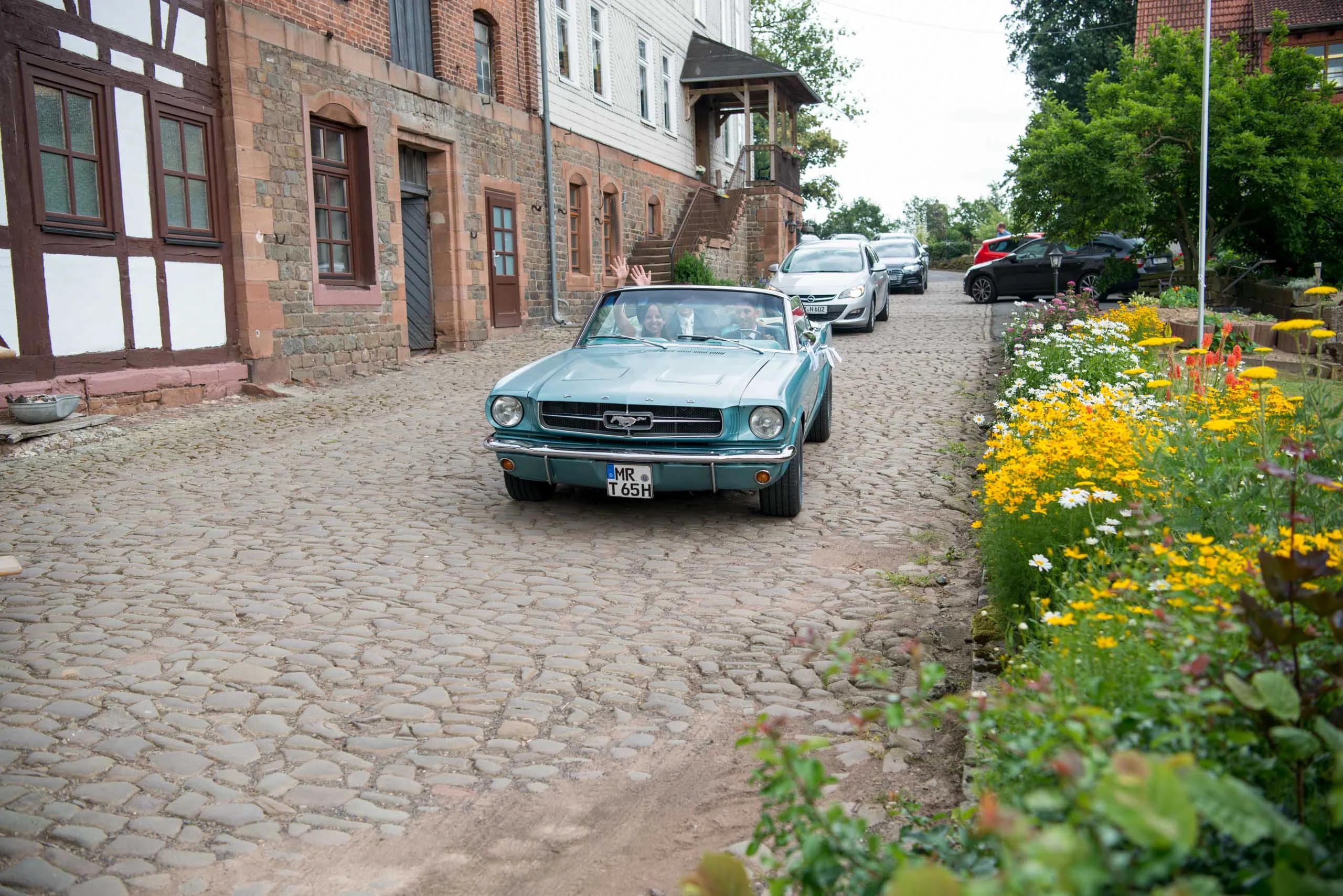Hochzeitsfeier Fotogalerie 009 | Peter Lauritis Photography Türkises Oldtimer-Cabrio fährt durch eine Gasse mit Kopfsteinpflaster