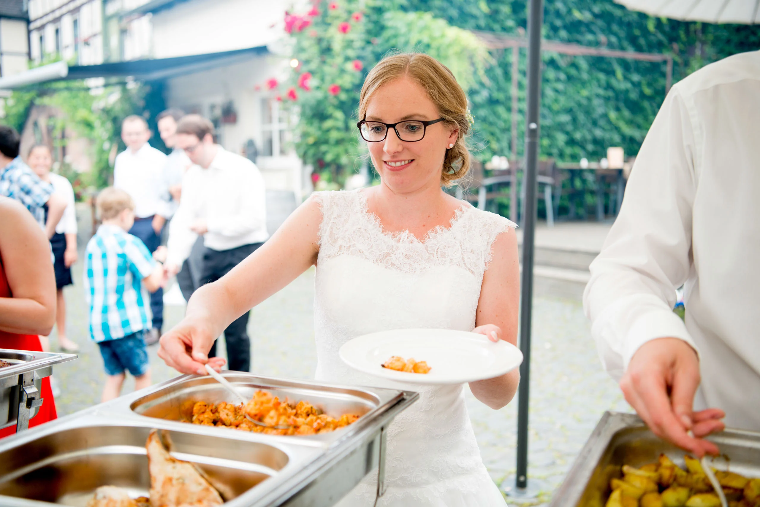 Hochzeitsfeier Fotogalerie 014 | Peter Lauritis Photography Braut mit Brille nimmt sich lächelnd Essen vom Buffet