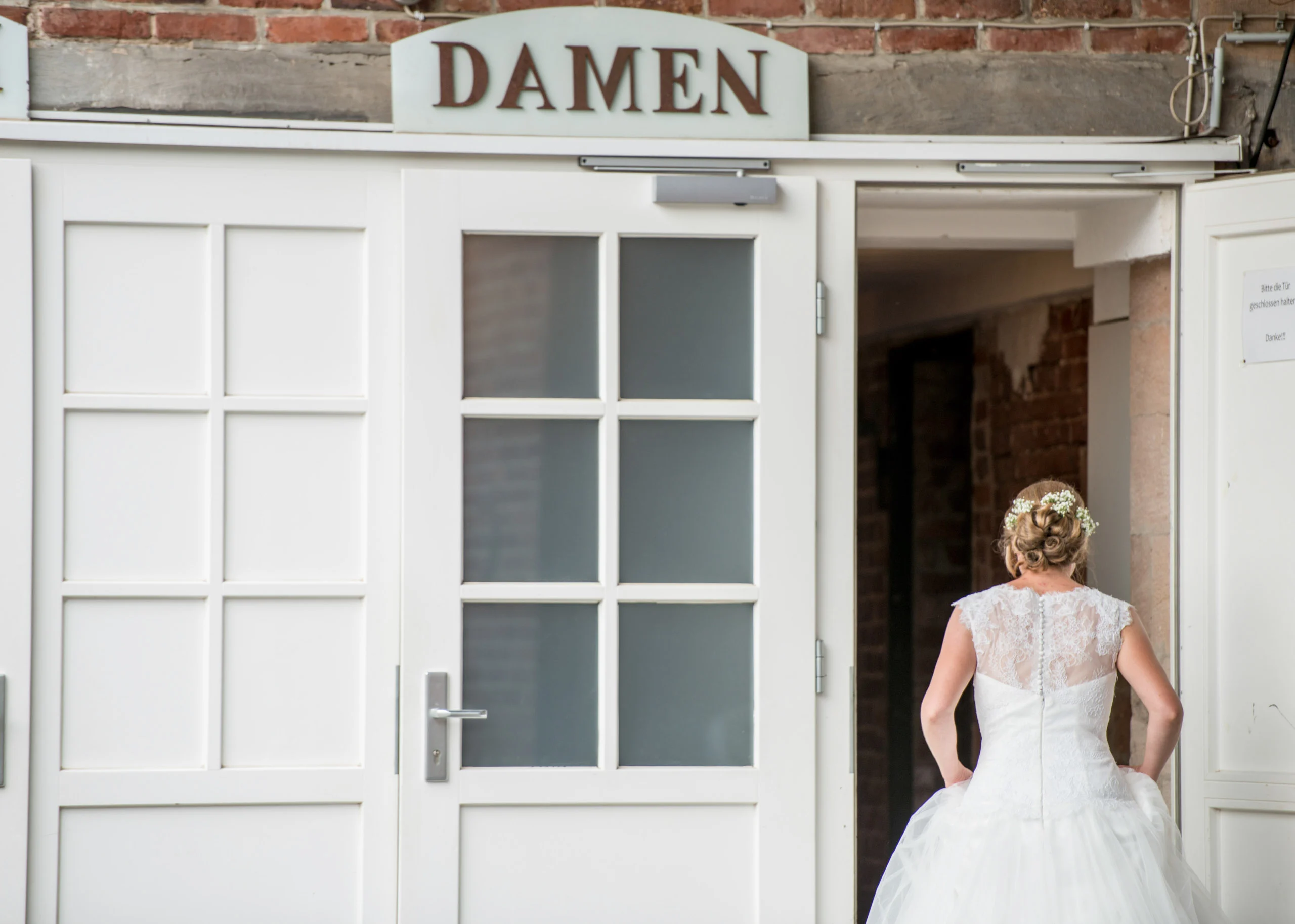 Hochzeitsfeier Fotogalerie 020 | Peter Lauritis Photography Braut geht durch eine weiße Tür mit dem Schild „Damen“
