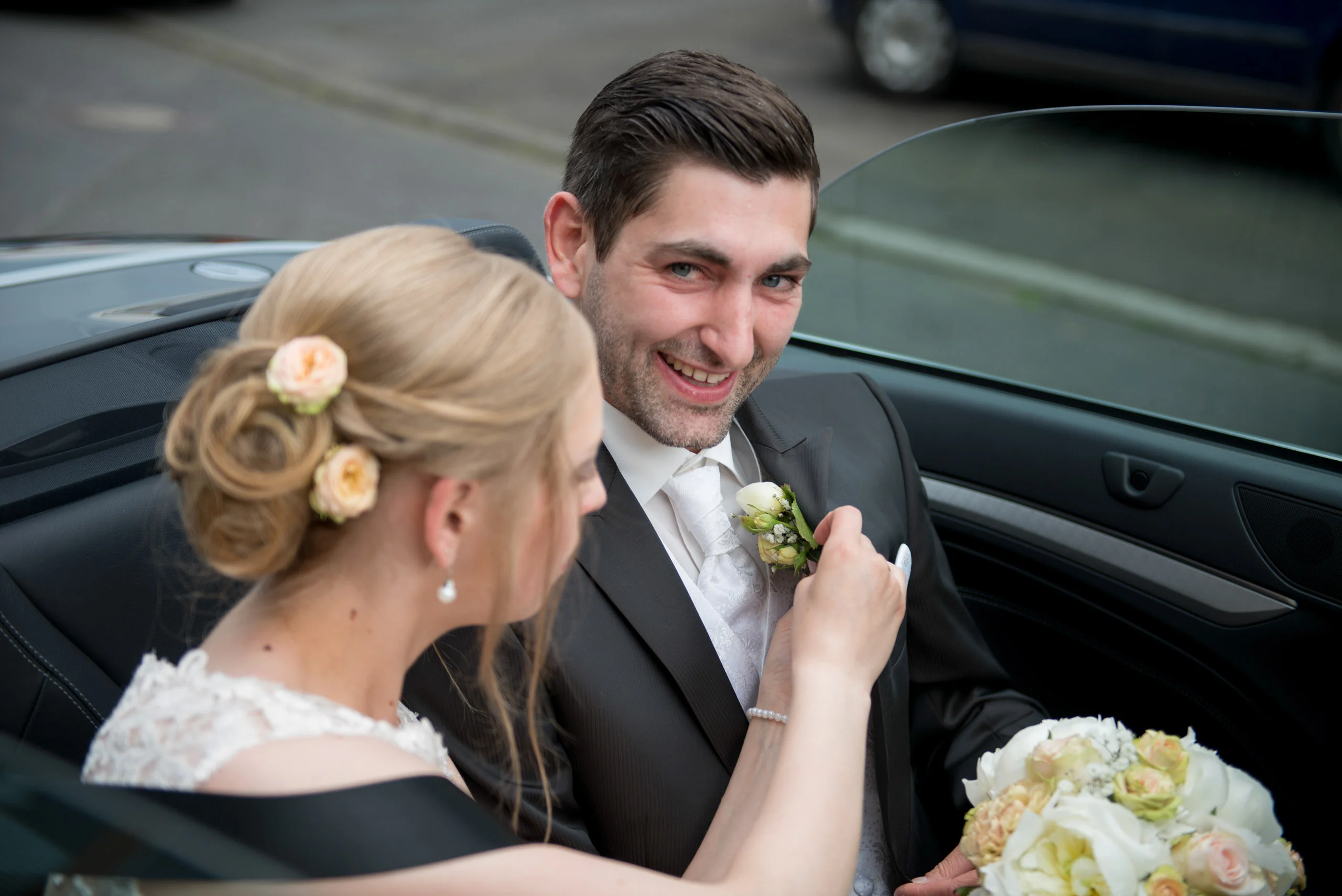 Hochzeitsfeier Fotogalerie 050 | Peter Lauritis Photography Braut steckt dem Bräutigam im Cabrio die Anstecknadel an