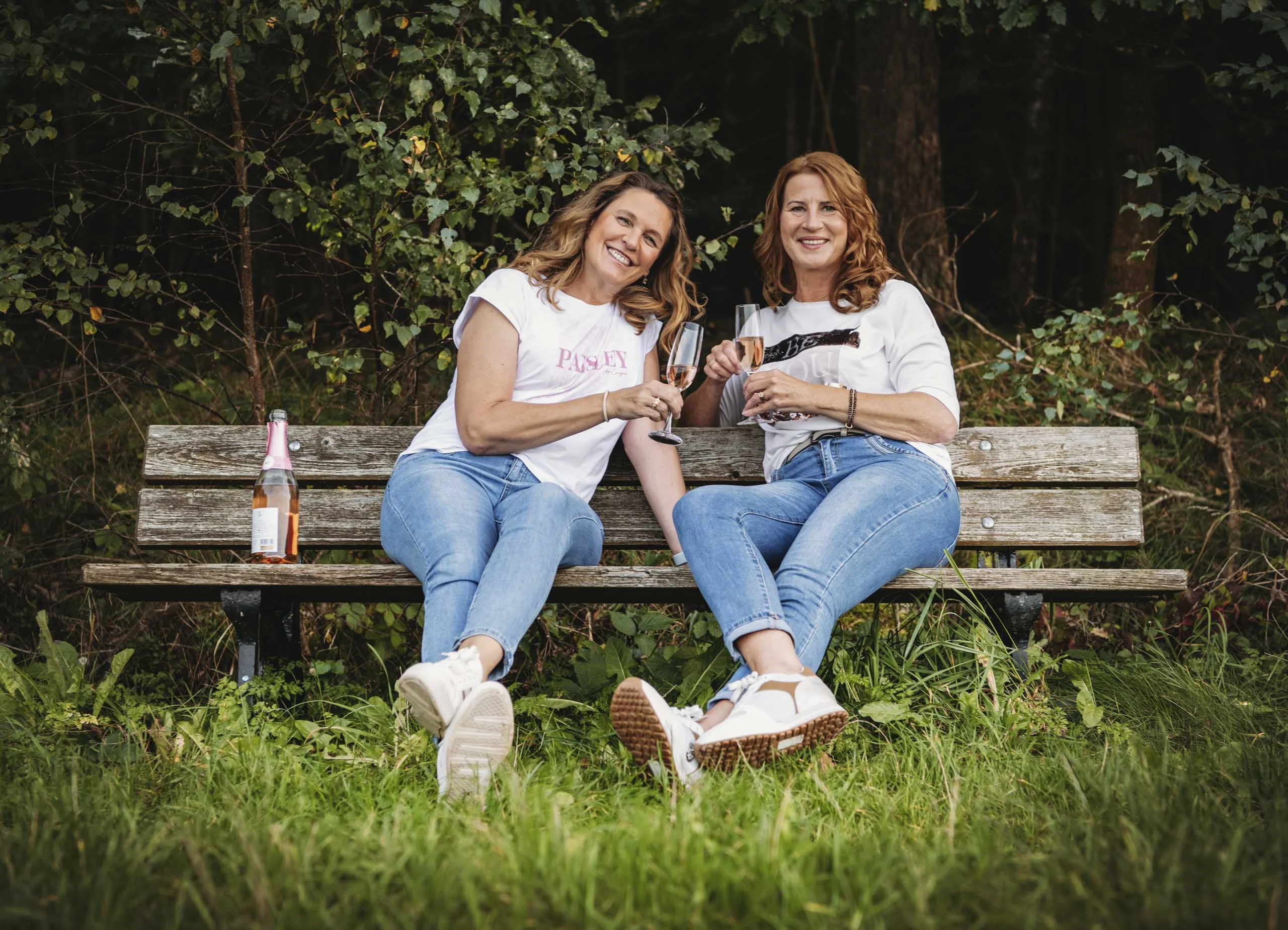 Best-Friends-Fotoshooting auf der Holzbank: zwei Freundinnen stoßen mit Gläsern an