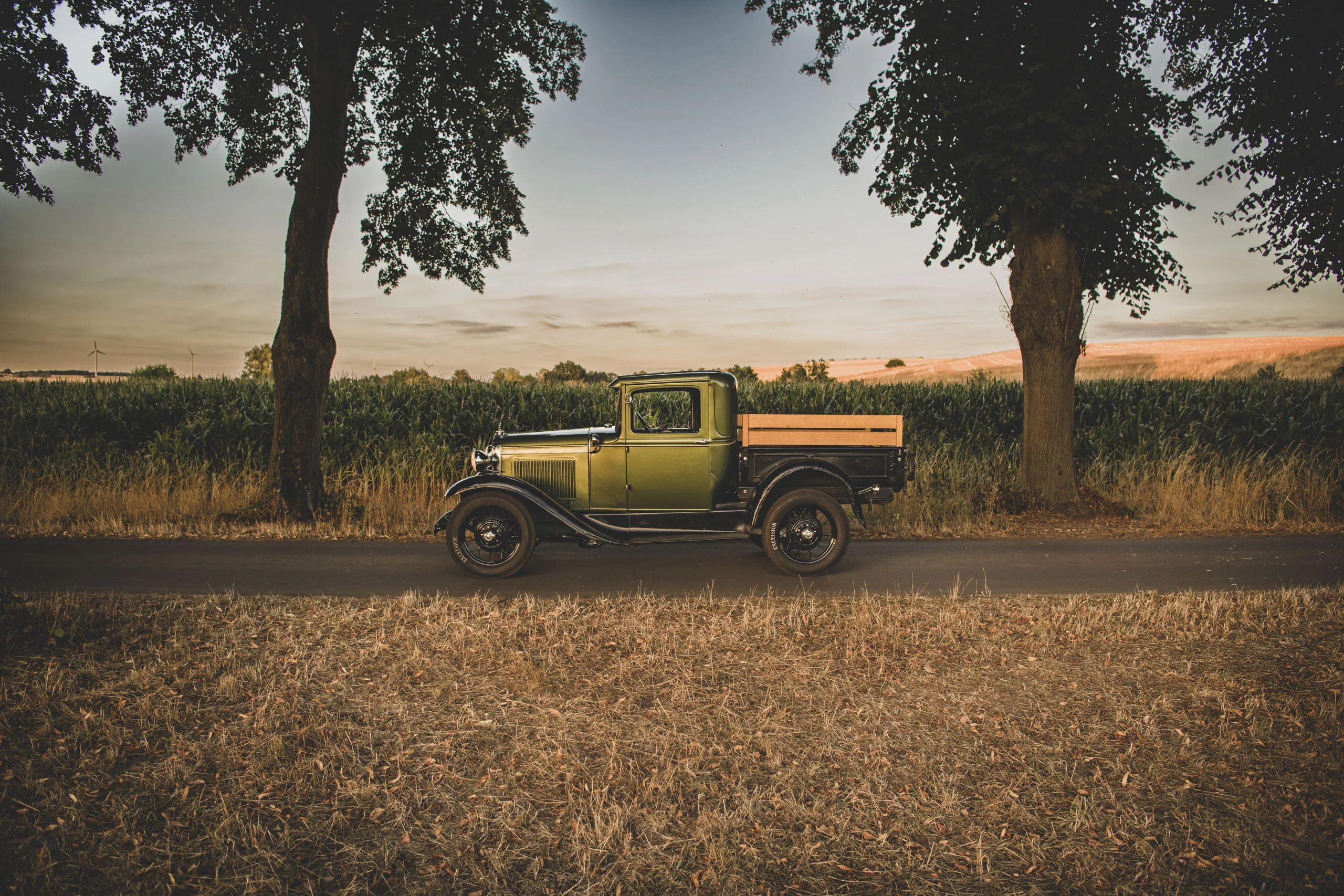 Auto-Fotoshooting: Oldtimer-Pick-up zwischen zwei großen Bäumen vor einem Feld