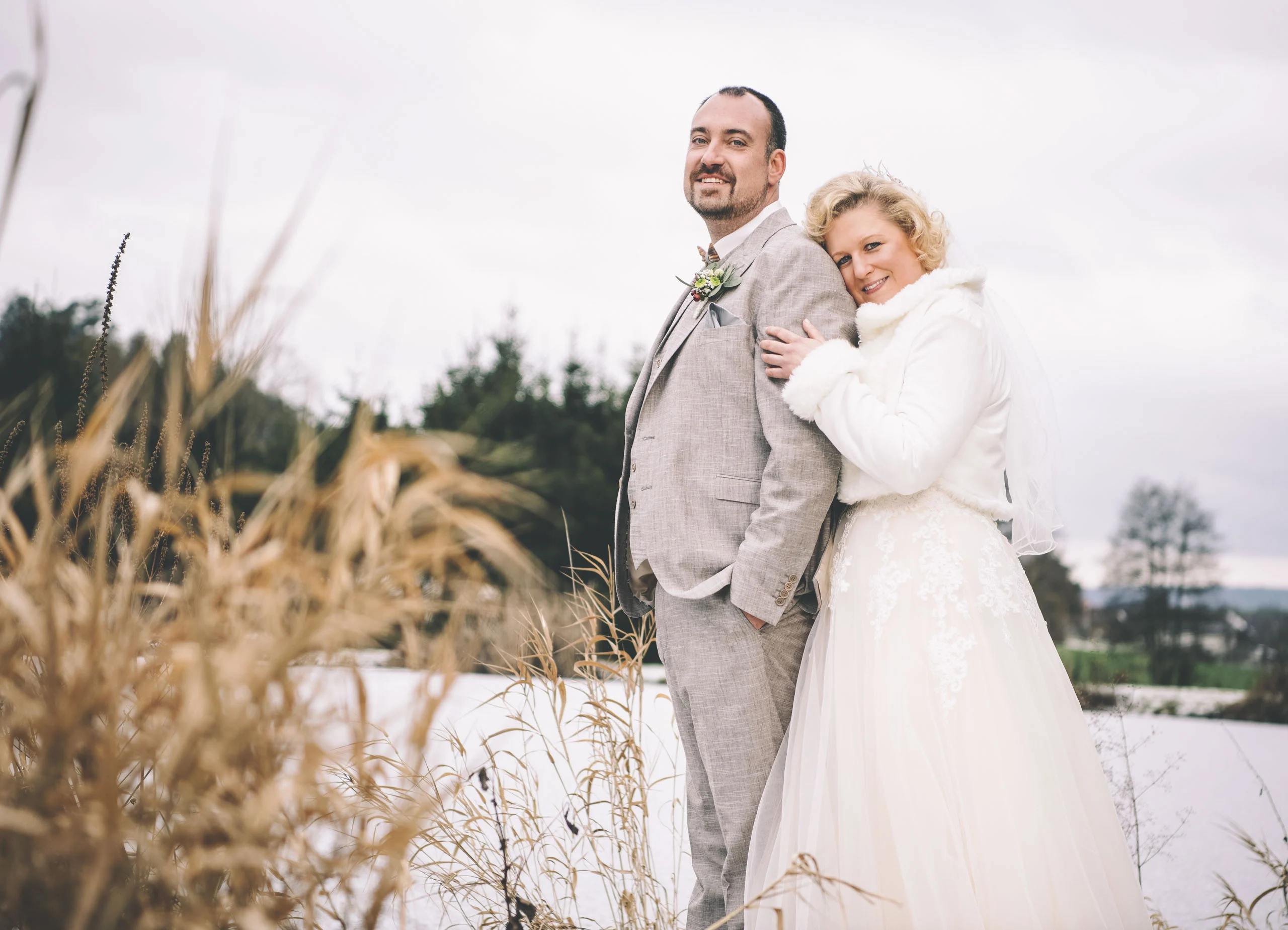 Hochzeitsshooting im Winter: Braut schmiegt sich an den Bräutigam, vorne goldene Gräser