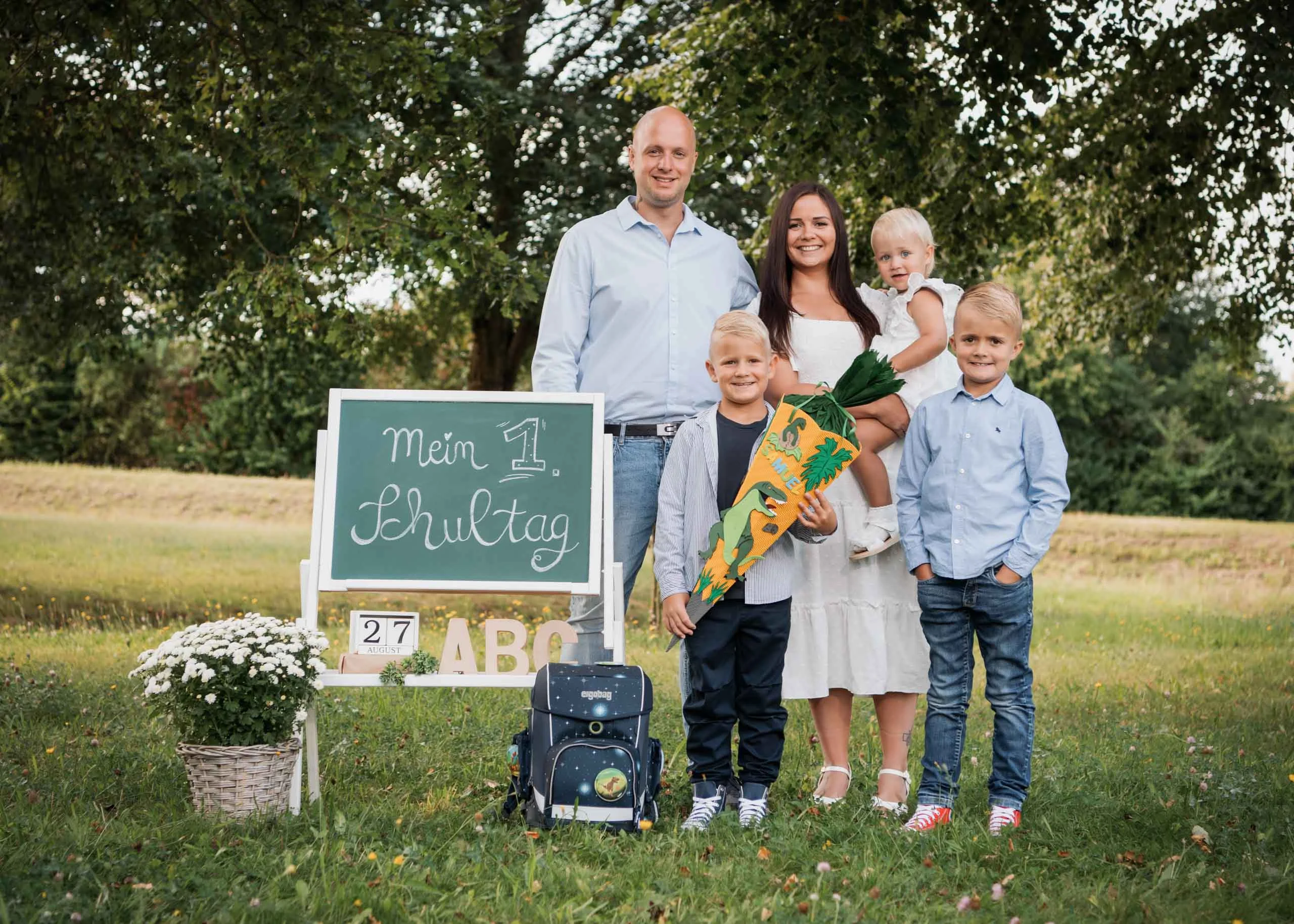 Einschulungsfotos Aktion 01 | Peter Lauritis Photography Familie mit drei Kindern steht zur Einschulung im Grünen neben einer Tafel „Mein 1. Schultag“, ein Junge hält die Schultüte