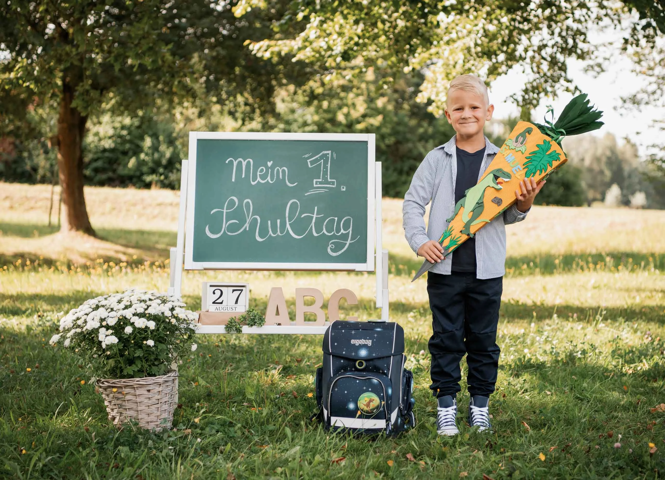 Einschulungsfotos Aktion 03 | Peter Lauritis Photography Schulkind mit Schultüte steht neben einer Tafel „Mein 1. Schultag“, davor Schulranzen und Blumenkorb