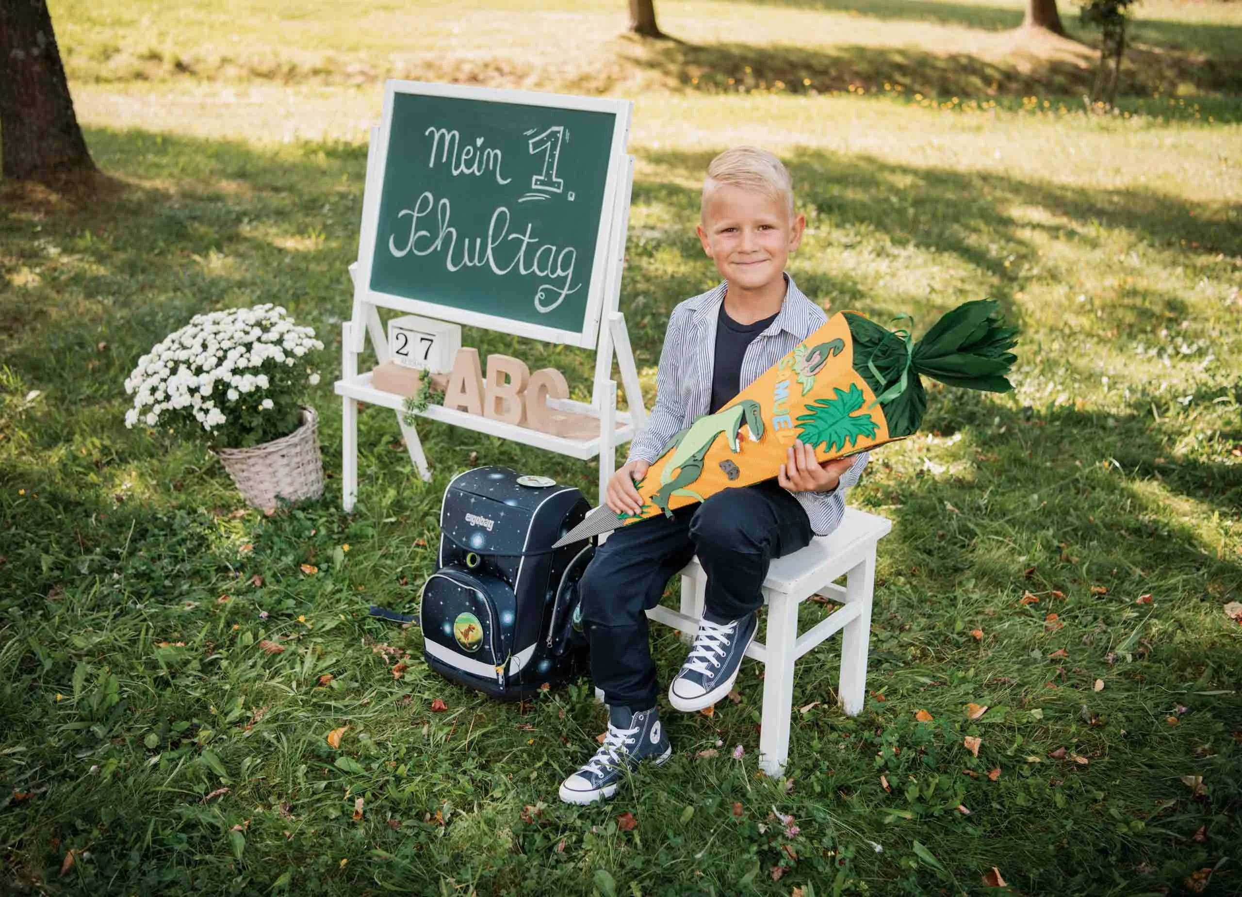 Einschulungsfotos Aktion 04 | Peter Lauritis Photography Junge sitzt mit Schultüte auf einem weißen Stuhl neben Tafel, Schulranzen und Blumen auf der Wiese