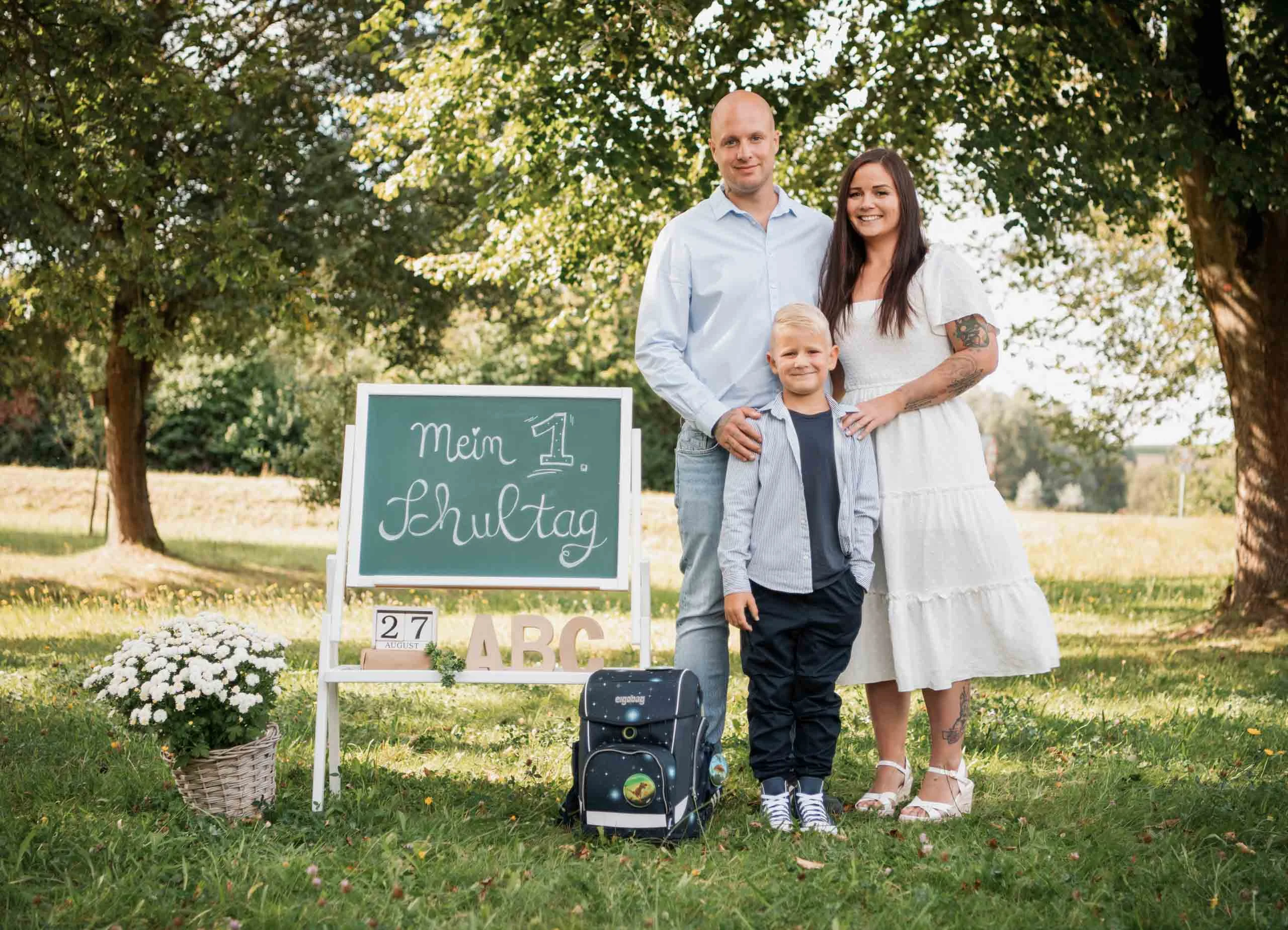 Einschulungsfotos Aktion 06 | Peter Lauritis Photography Eltern stehen mit ihrem Schulkind auf der Wiese neben Tafel und Schulranzen