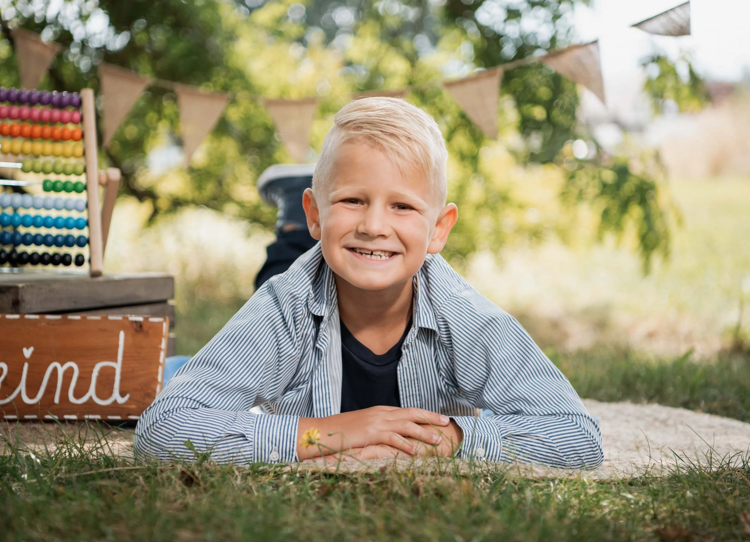 Einschulungsfotos Aktion 09 | Peter Lauritis Photography Lachender Junge liegt auf dem Bauch vor einem Holzschild „Schulkind“