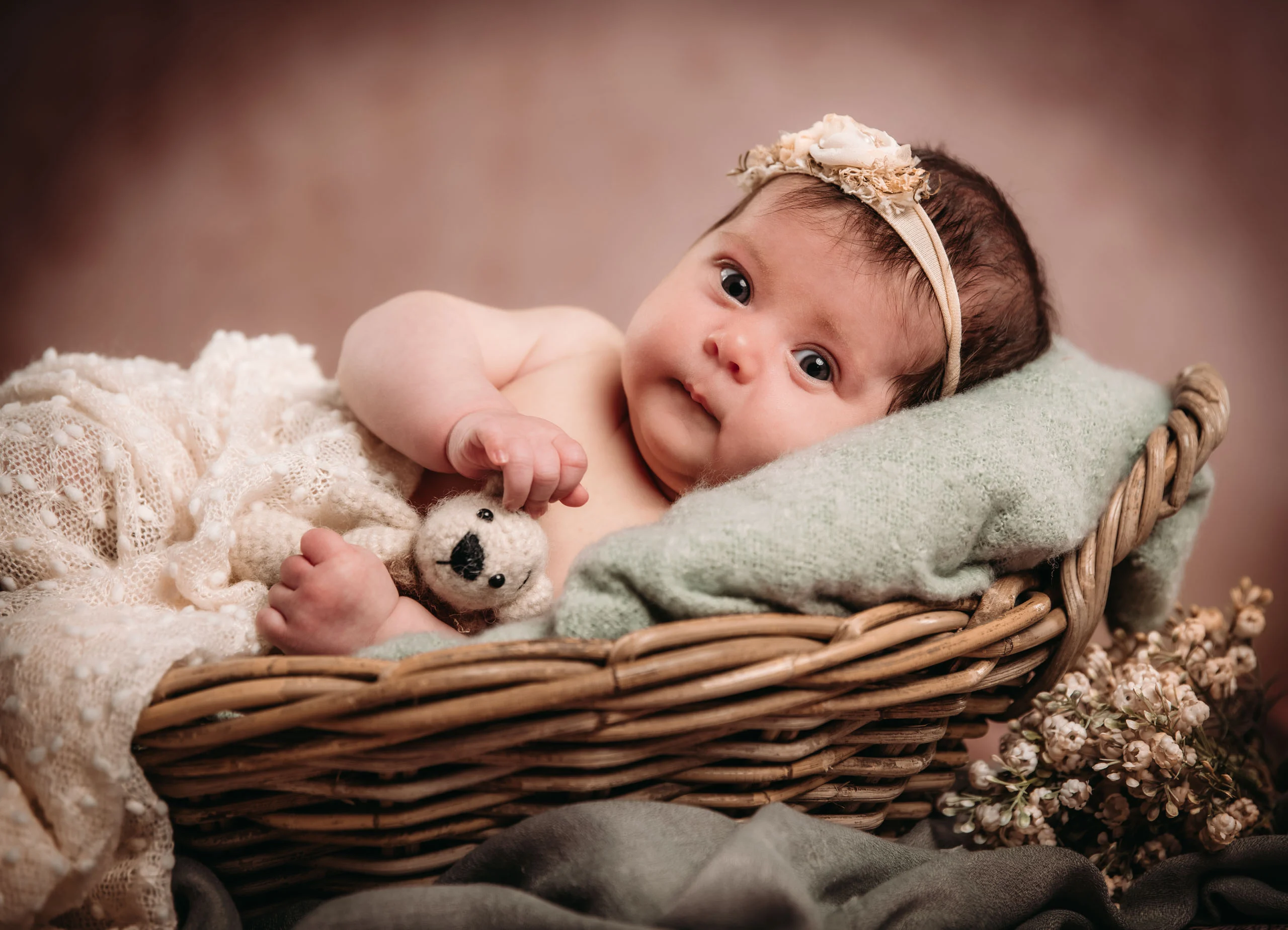 Baby- und Newbornfotos Produktbild 01 | Peter Lauritis Photography Baby mit Blumen-Haarband liegt in einem Weidenkorb mit mintgrüner Decke und kleinem Teddy