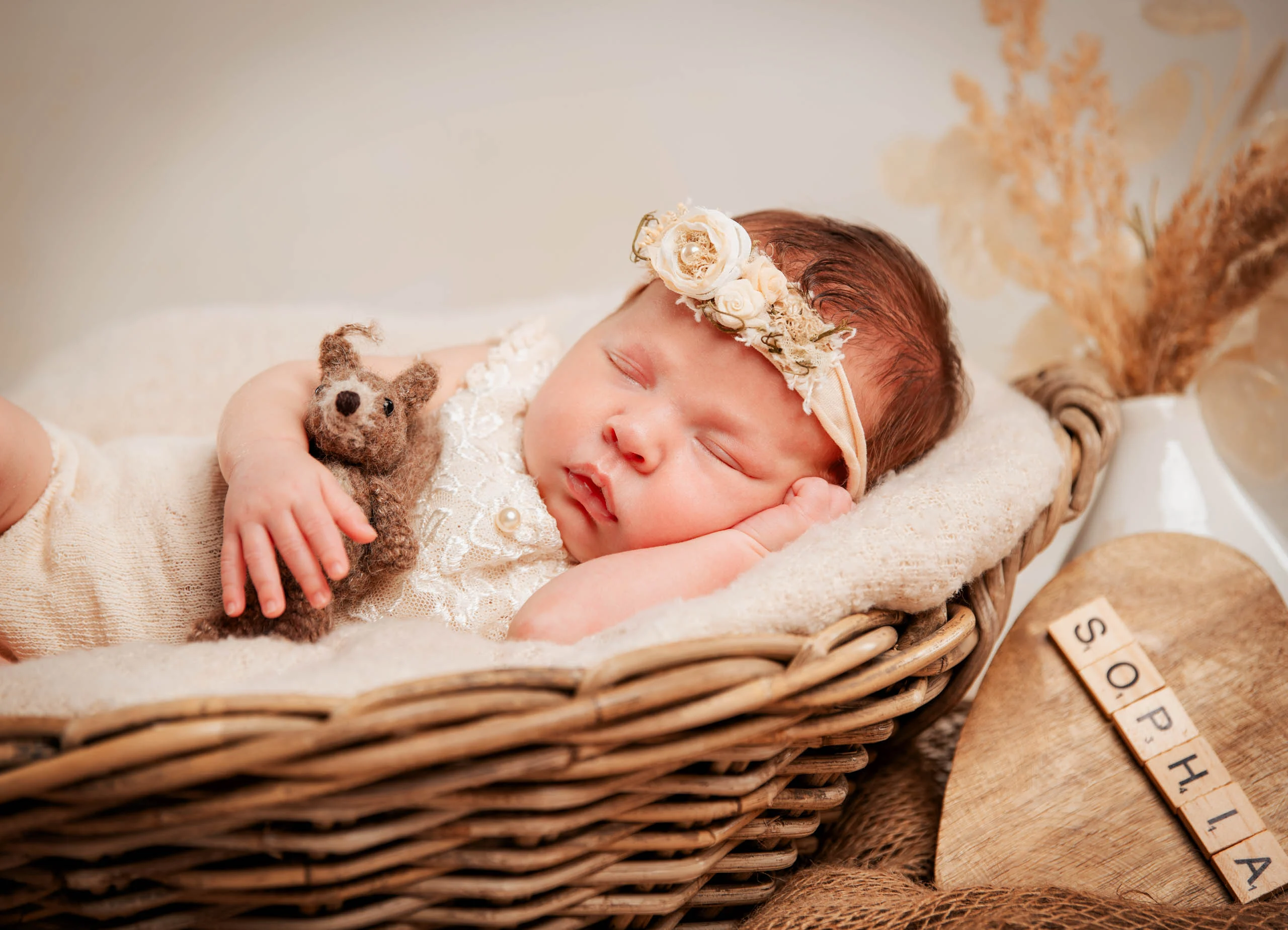 Baby- und Newbornfotos Produktbild 06 | Peter Lauritis Photography Schlafendes Neugeborenes mit Blumen-Haarband und kleinem Strickhasen im Weidenkorb