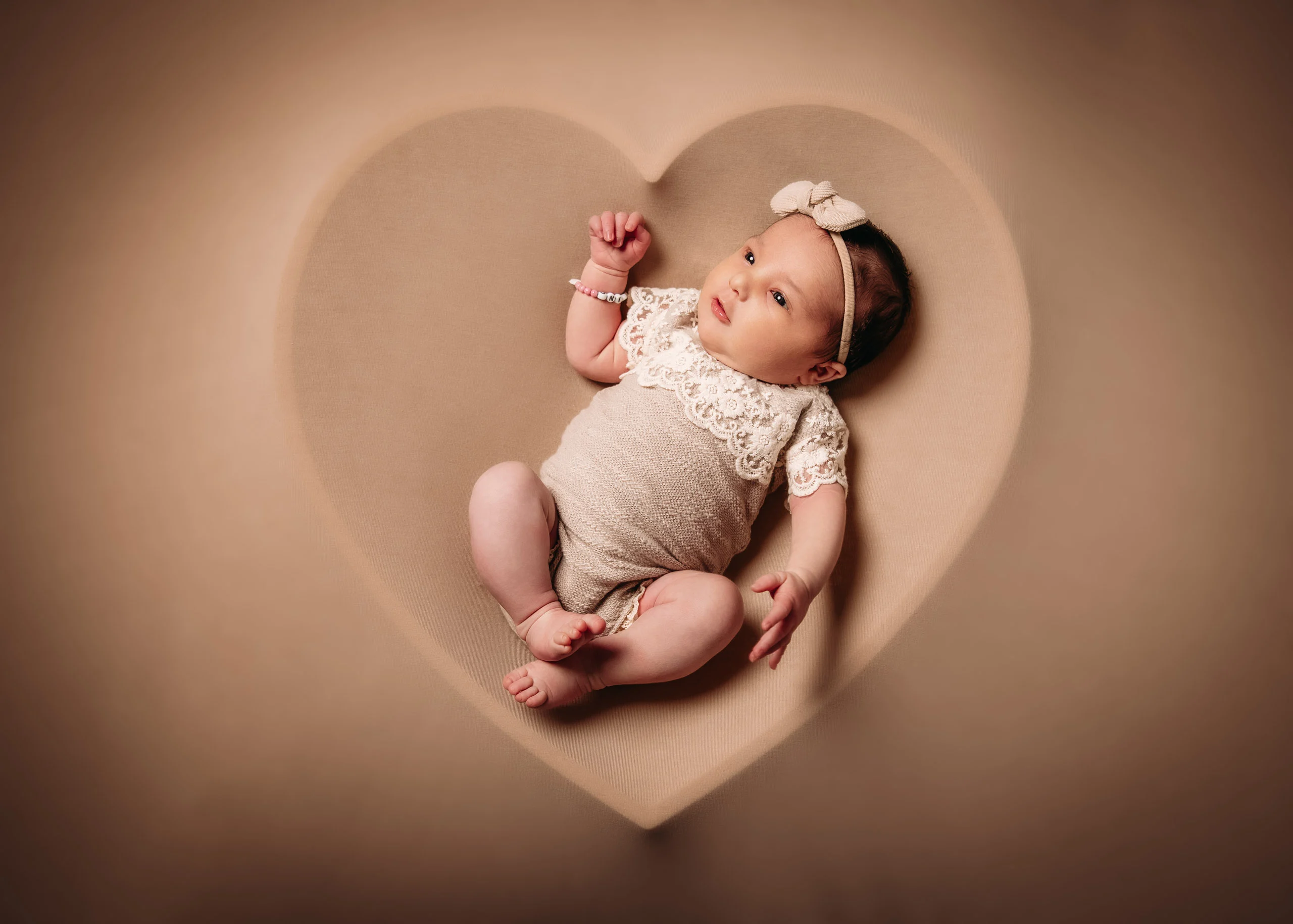 Baby- und Newbornfotos Produktbild 08 | Peter Lauritis Photography Baby im Spitzenbody liegt in einer herzförmigen Mulde auf beigem Hintergrund