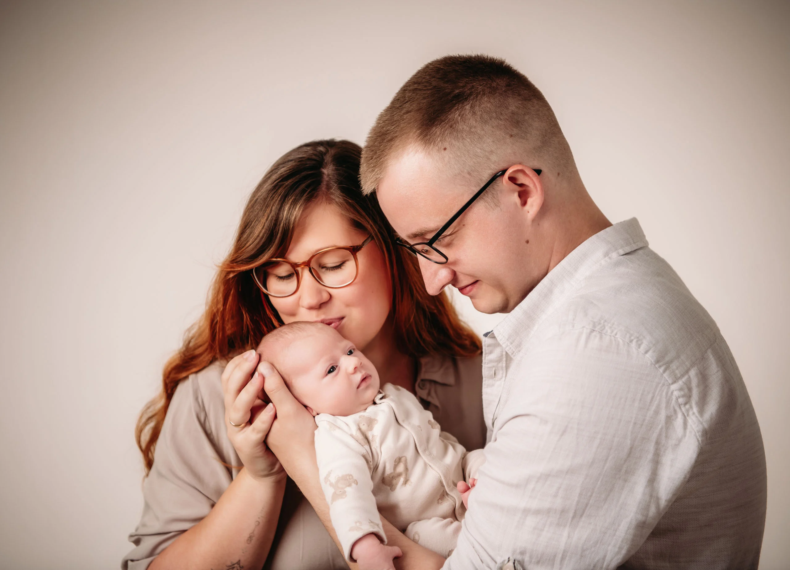 Baby- und Newbornfotos Produktbild 11 | Peter Lauritis Photography Eltern mit Brille kuscheln ihr Neugeborenes zwischen sich