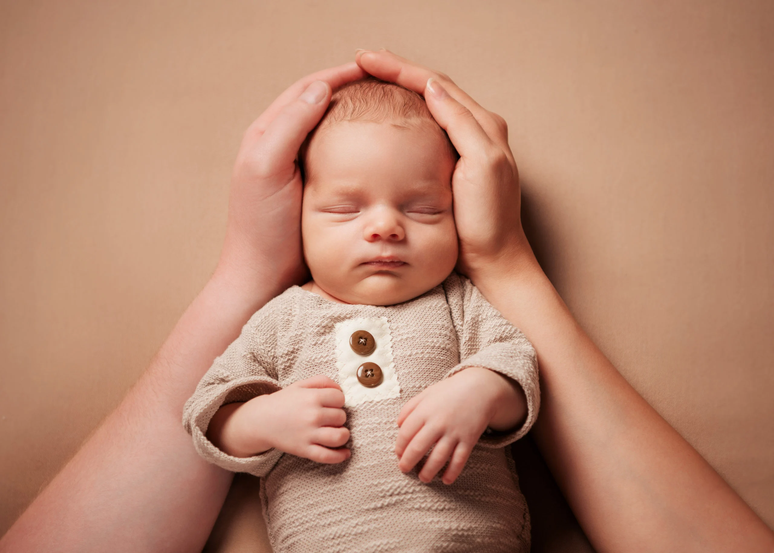 Baby- und Newbornfotos Produktbild 14 | Peter Lauritis Photography Erwachsenenhände halten den Kopf eines schlafenden Neugeborenen im Strickbody