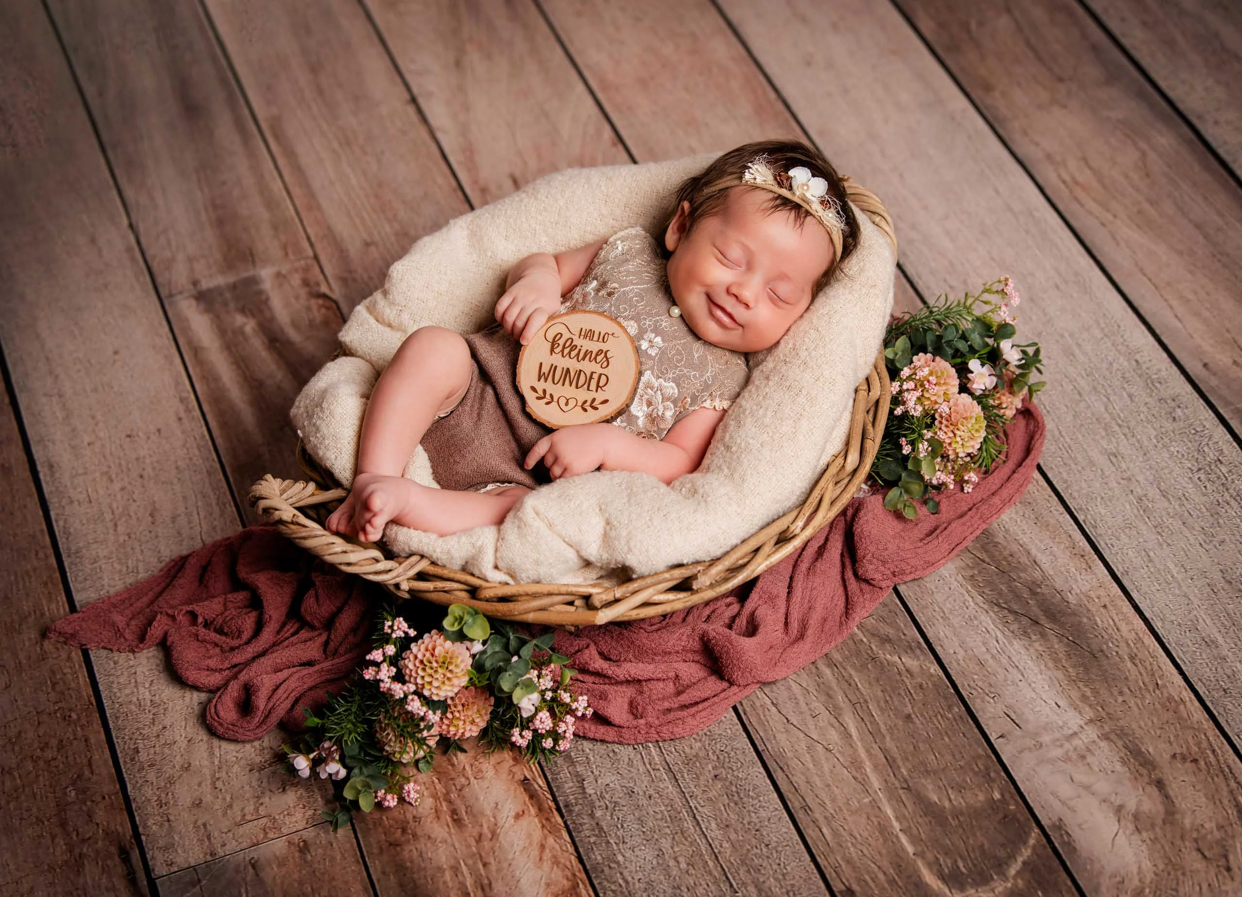 Baby- und Newbornfotos Produktbild 17 | Peter Lauritis Photography Schlafendes Neugeborenes mit Holzschild im Weidenkorb, von oben auf Holzboden fotografiert