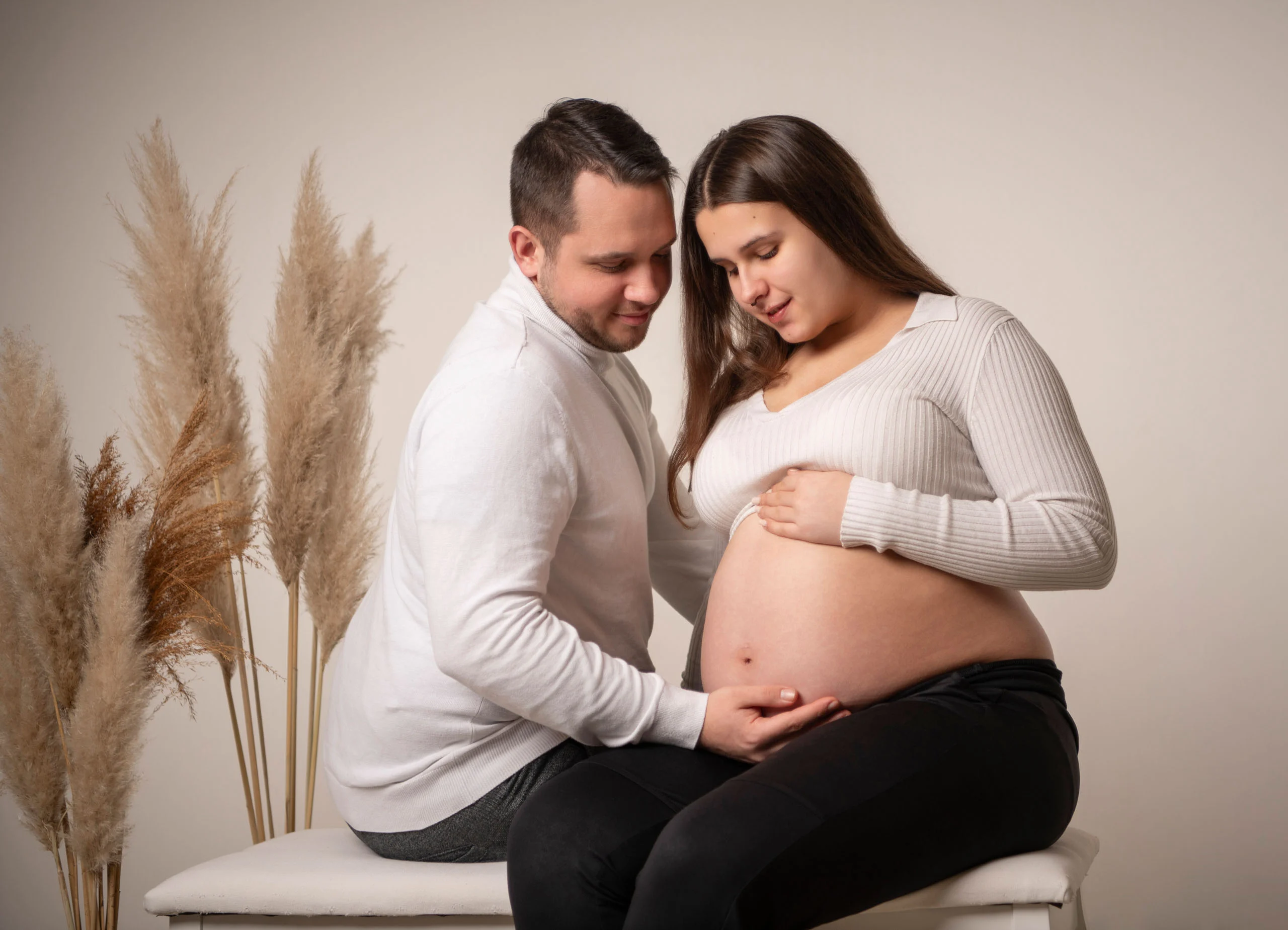 Babybauch Komplettpaket Produktbild 01 | Peter Lauritis Photography Paar sitzt vor Pampasgras, beide legen die Hände auf den Babybauch