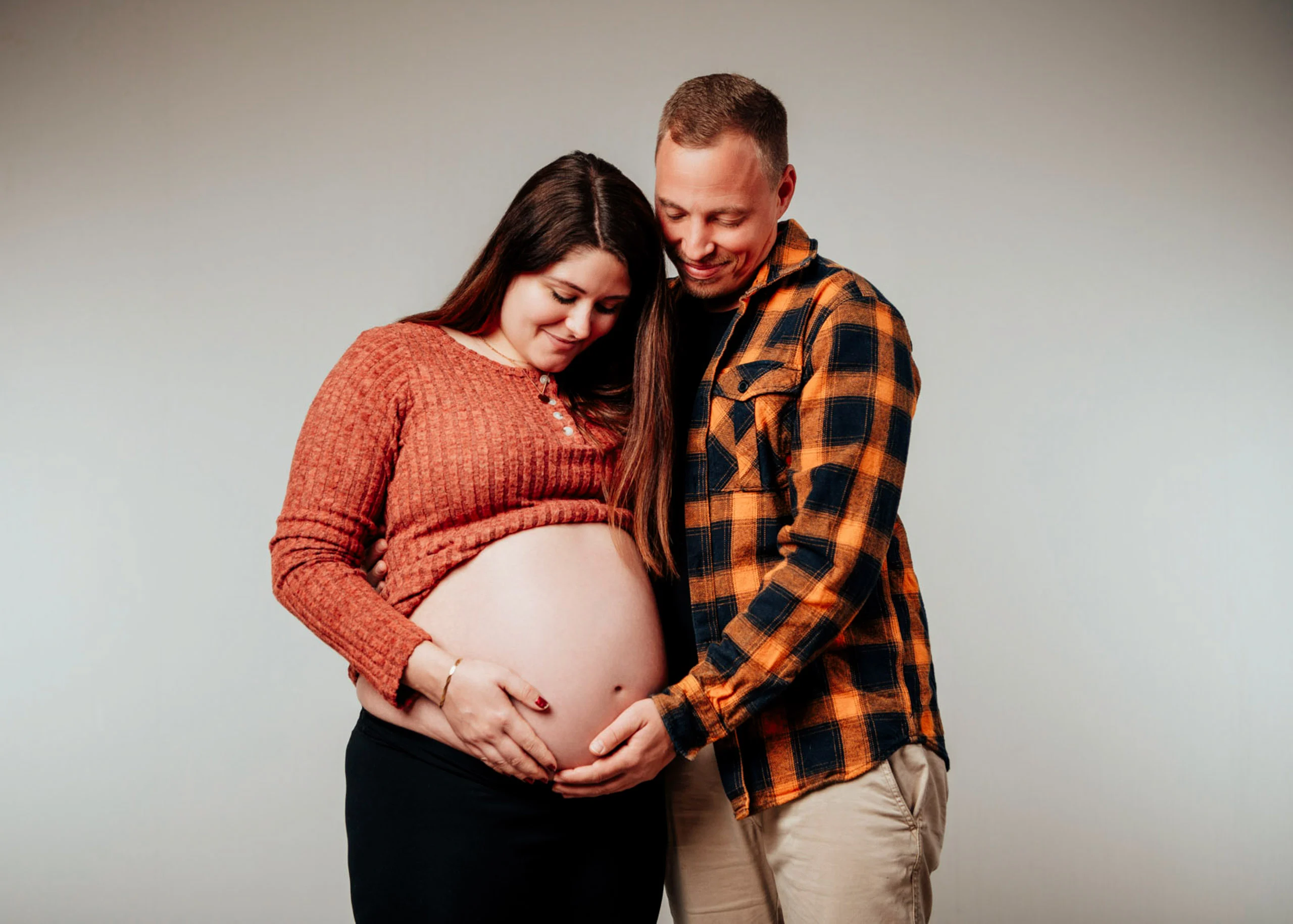 Babybauch Komplettpaket Produktbild 07 | Peter Lauritis Photography Schwangere im orangen Pullover und Mann im karierten Hemd halten gemeinsam den Babybauch