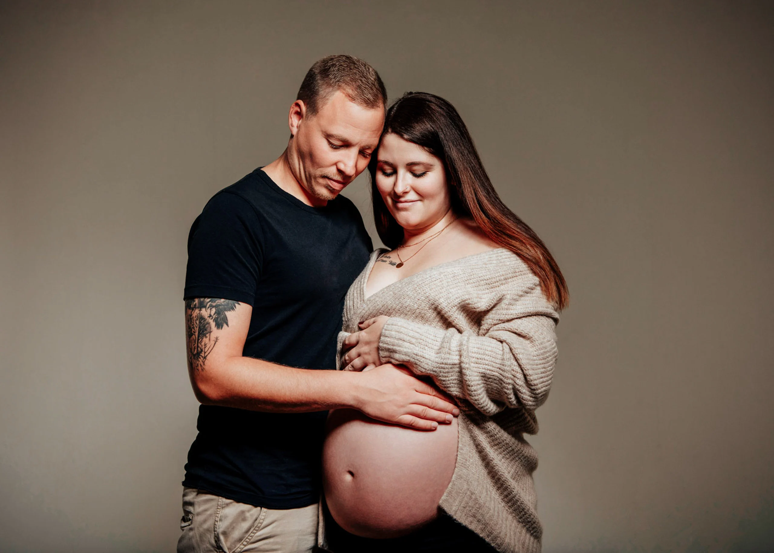 Paar blickt gemeinsam auf den Babybauch, er umarmt sie von der Seite