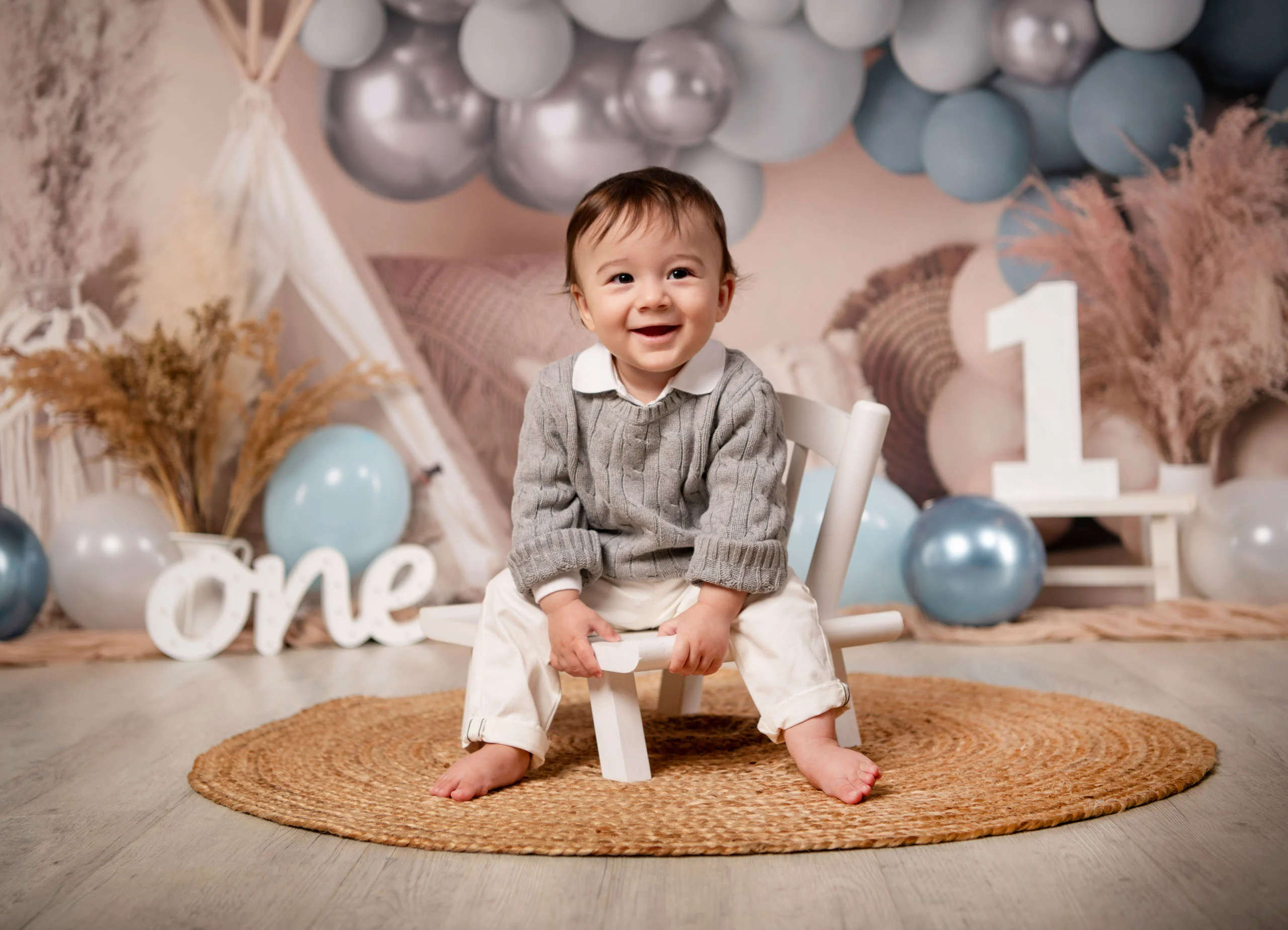 Cake Smash Produktbild 02 | Peter Lauritis Photography Kleiner Junge sitzt lachend auf einem Holzstühlchen vor blauen Luftballons und einer großen Eins