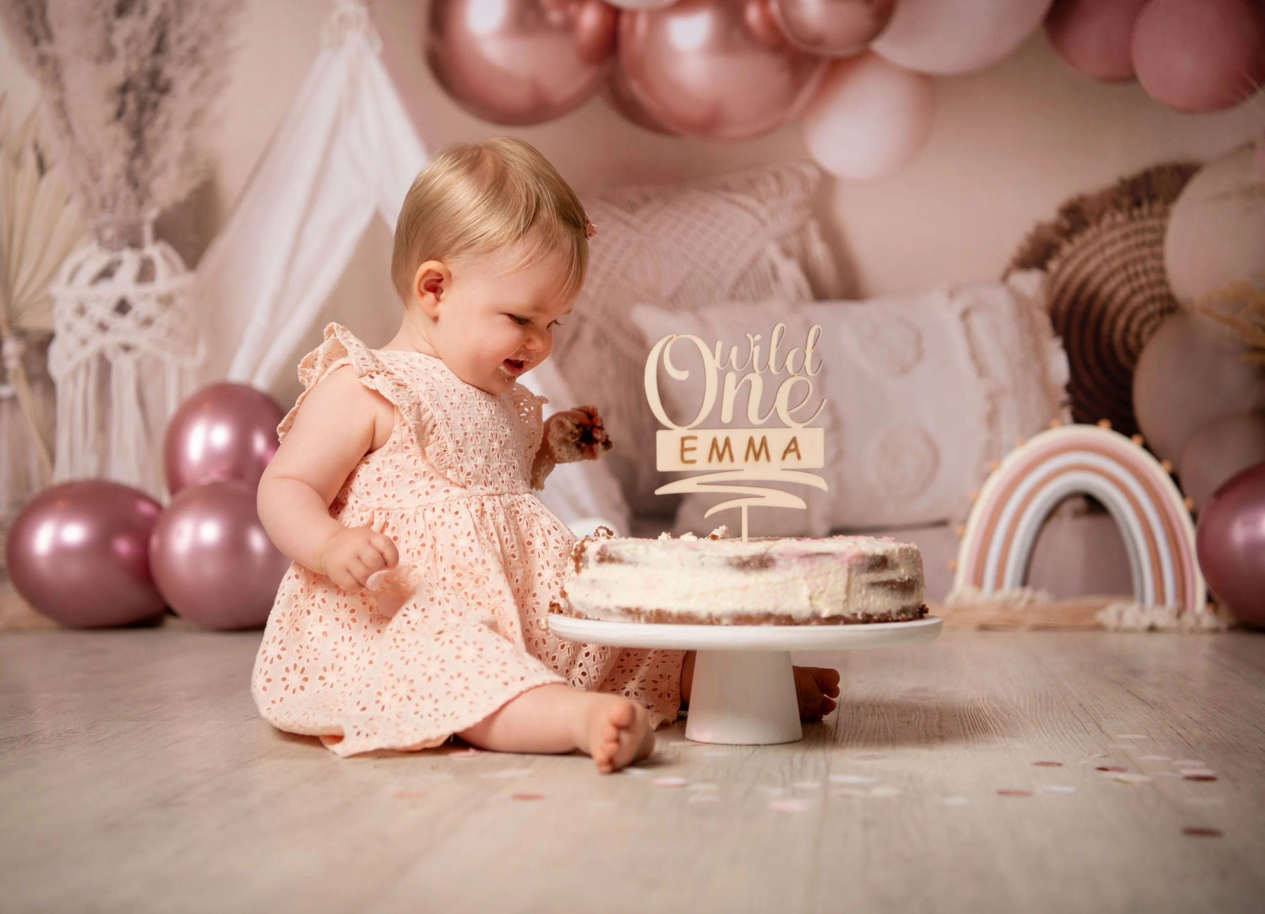 Cake Smash Produktbild 10 | Peter Lauritis Photography Mädchen im rosa Kleid greift in die Geburtstagstorte, dahinter Tipi und Regenbogen-Deko