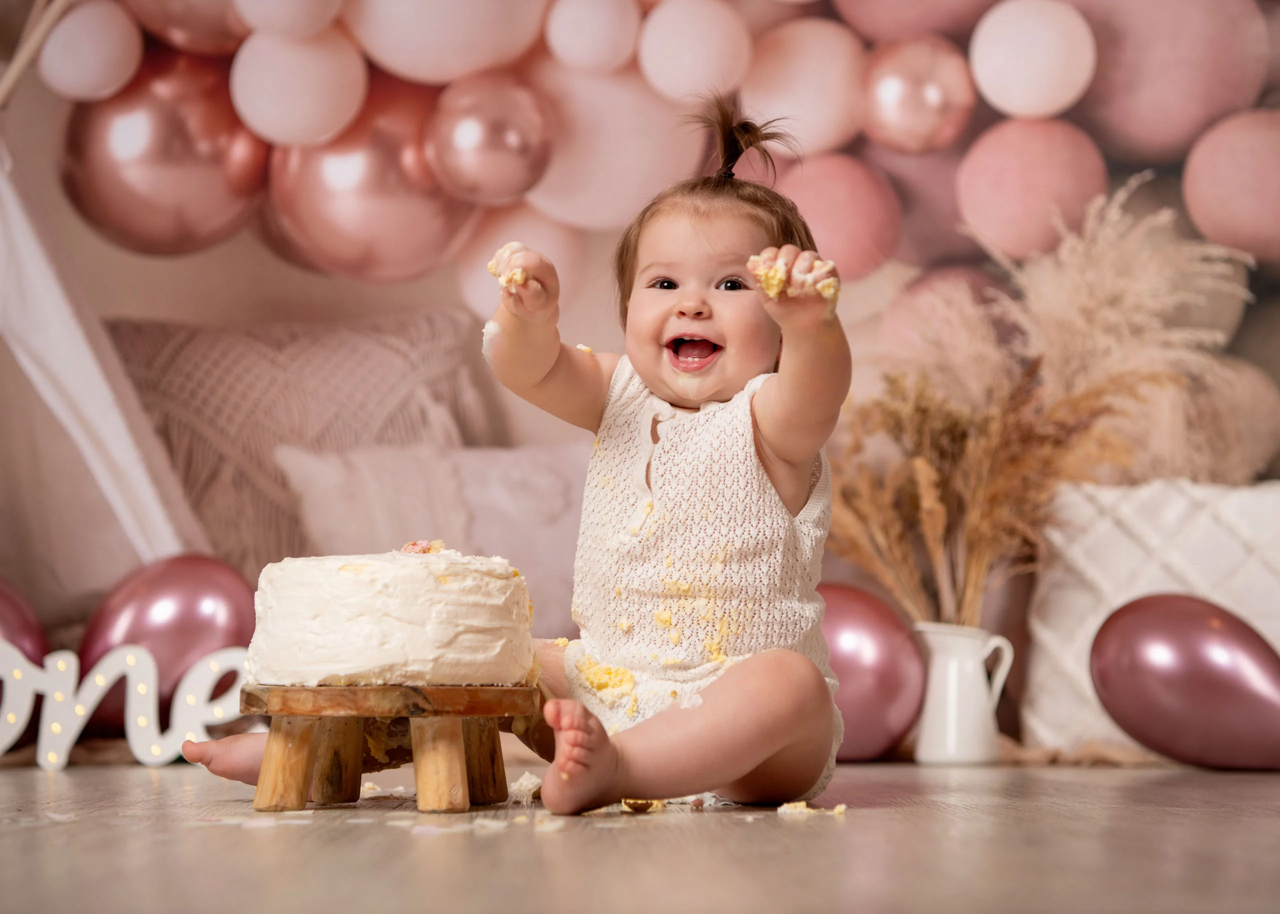 Cake Smash Produktbild 12 | Peter Lauritis Photography Lachendes Baby mit Haarzopf hebt die Hand mit Sahne, vor ihm die weiße Torte