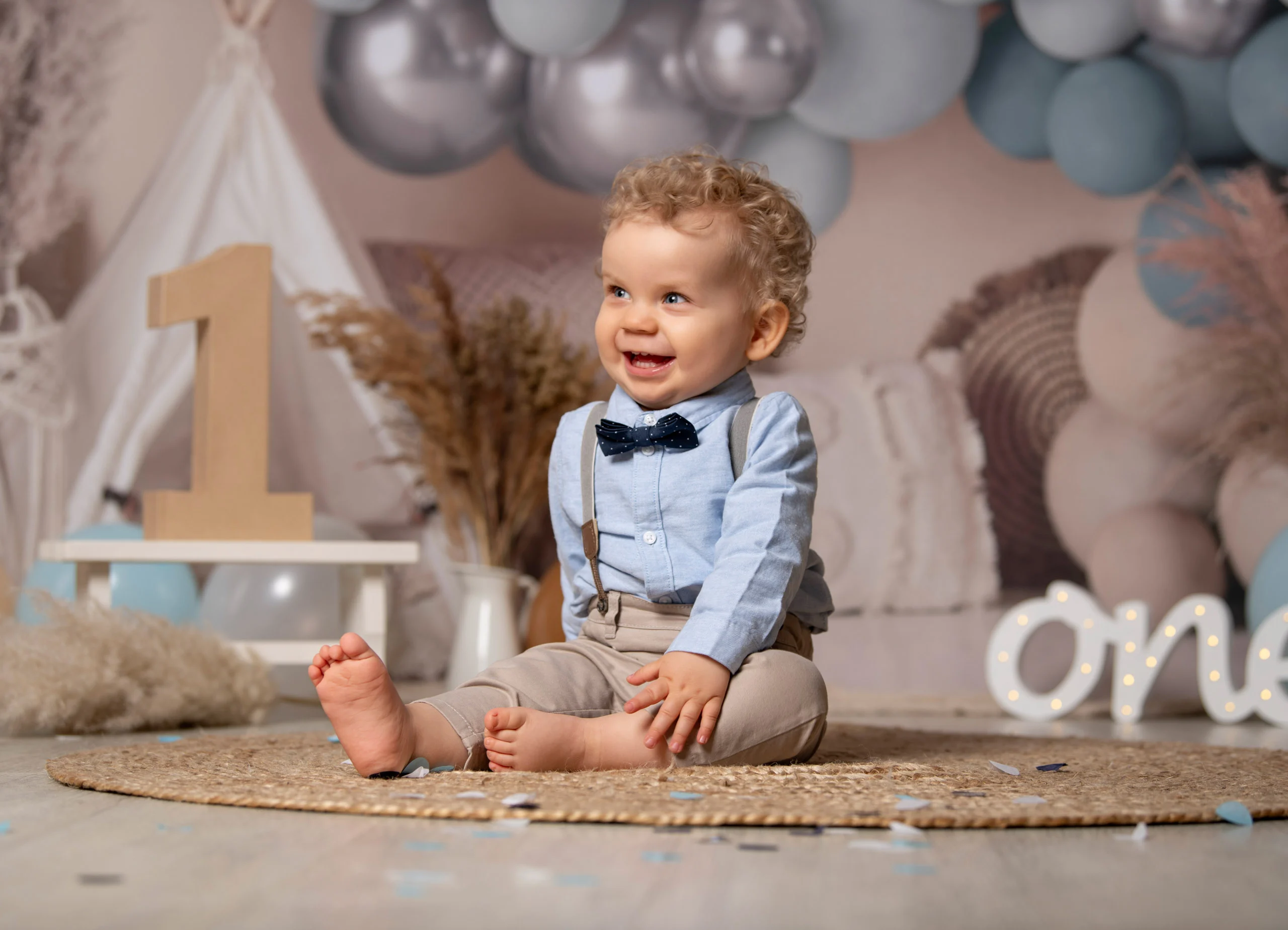 Cake Smash Produktbild 17 | Peter Lauritis Photography Kleiner Junge mit Fliege sitzt lachend auf einem Juteteppich neben einer großen Holz-Eins