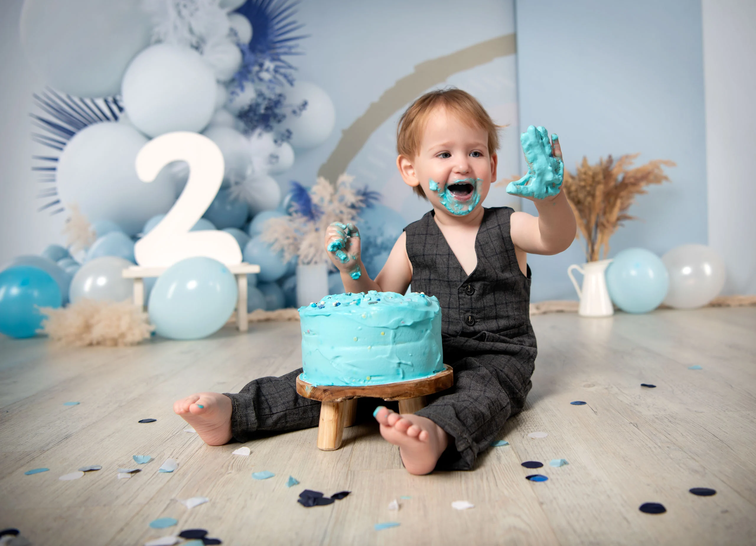 Cake Smash Produktbild 18 | Peter Lauritis Photography Kleinkind mit blauer Sahne im Gesicht hält die Hand hoch, vor ihm eine blaue Torte und eine große Zwei