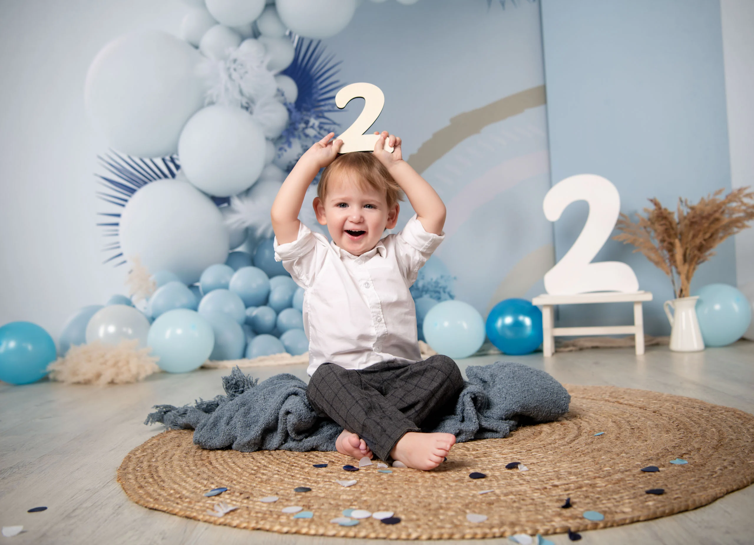 Cake Smash Produktbild 20 | Peter Lauritis Photography Lachender Junge hält eine weiße Zwei über den Kopf, sitzt vor blauer Ballonkulisse