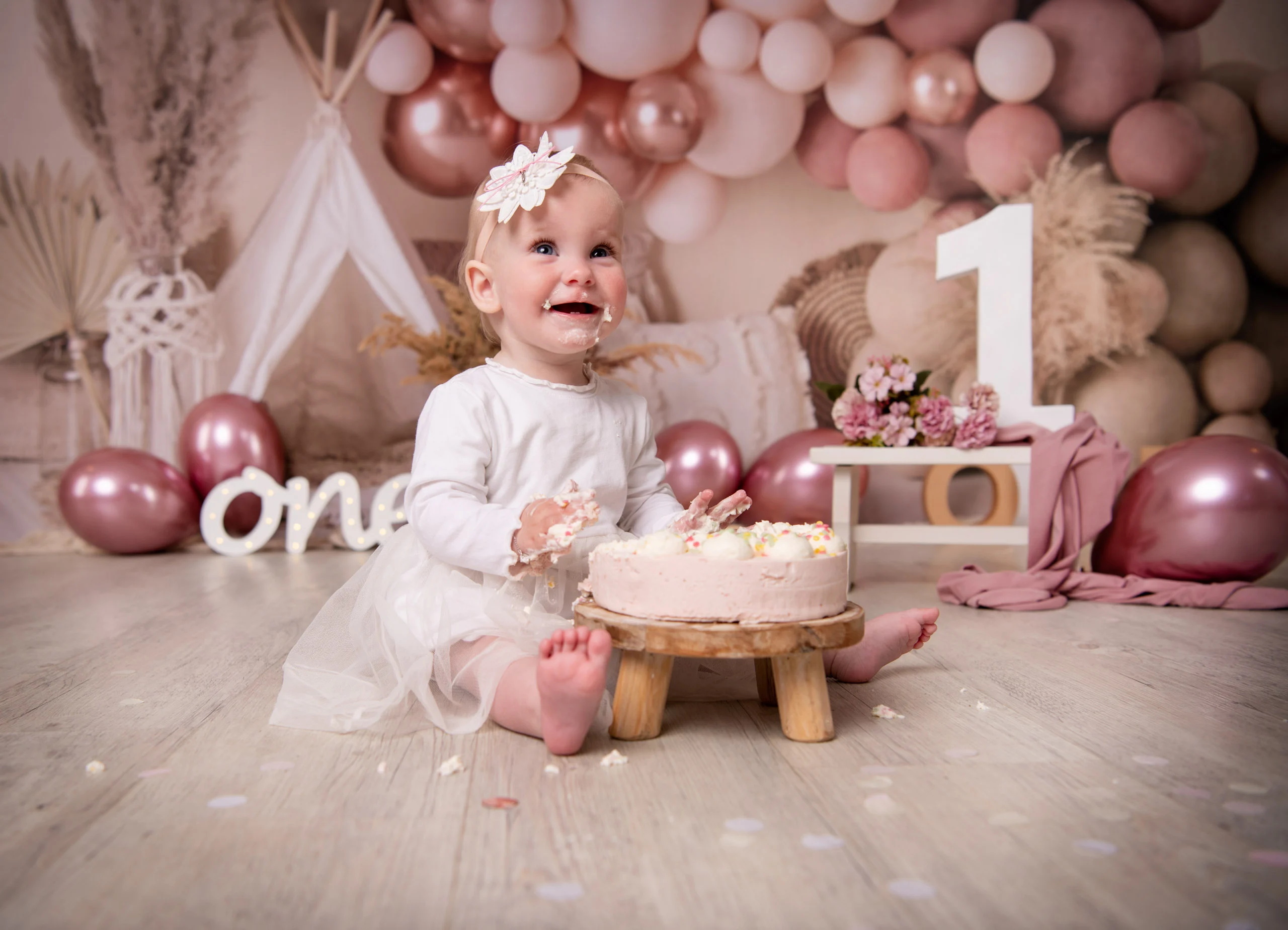 Cake Smash Produktbild 21 | Peter Lauritis Photography Kleines Mädchen im weißen Kleid sitzt lachend an einer rosa Torte vor Ballons
