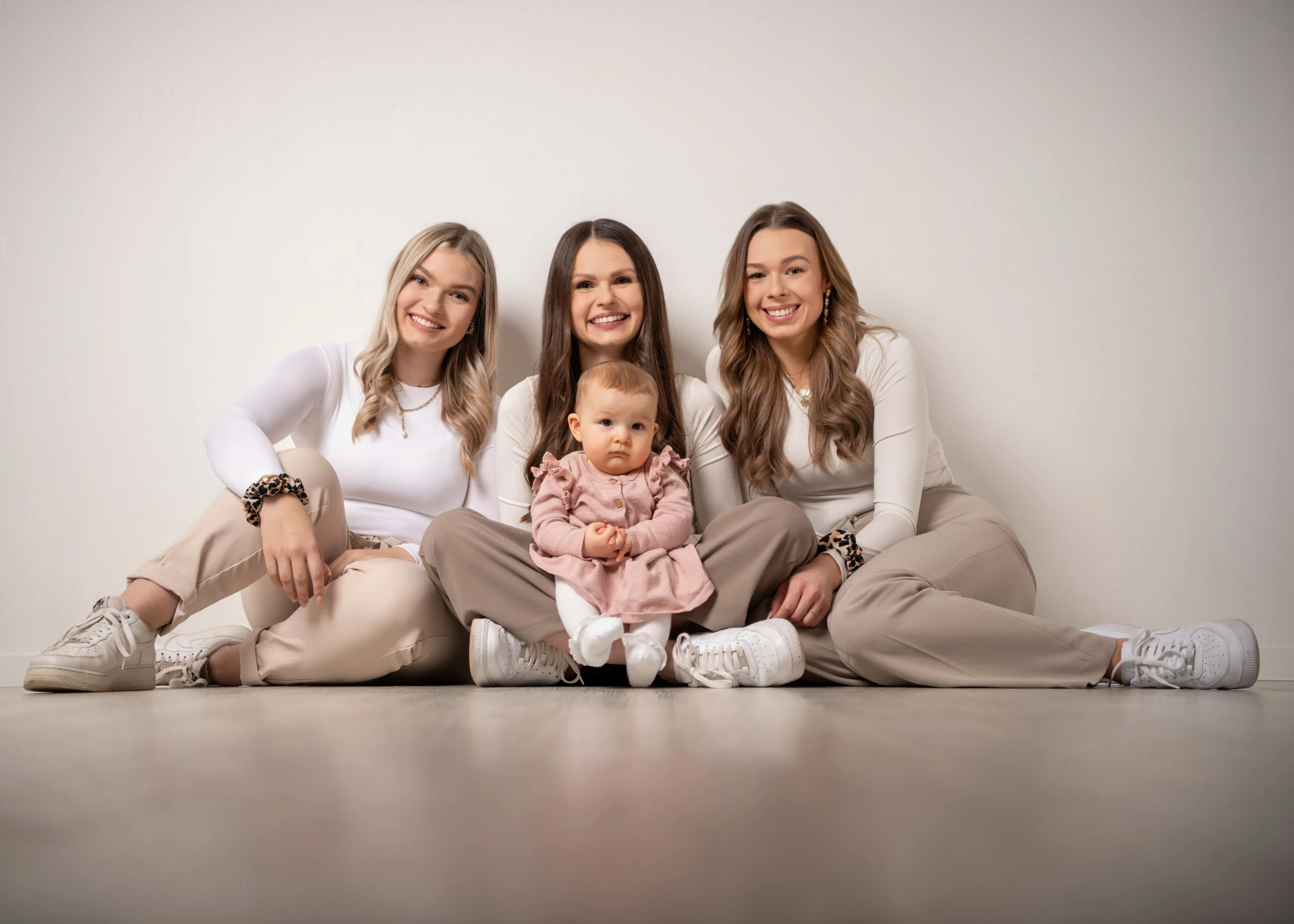 Familienfotos Produktbild 01 | Peter Lauritis Photography Drei junge Frauen sitzen auf dem Studioboden, in ihrer Mitte ein Baby im rosa Kleid