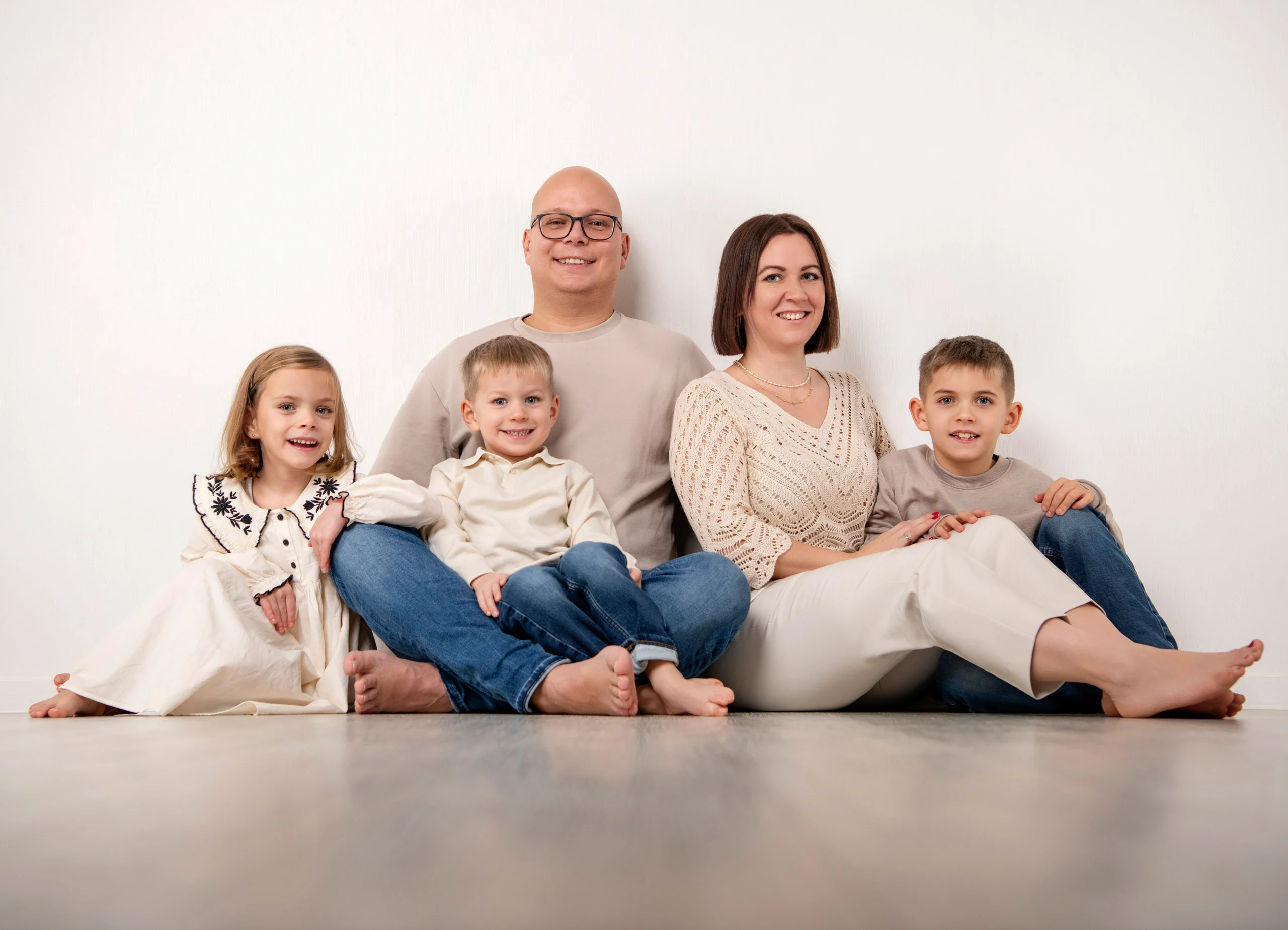 Familienfotos Produktbild 03 | Peter Lauritis Photography Familie mit drei Kindern sitzt barfuß in hellen Farben auf dem Studioboden