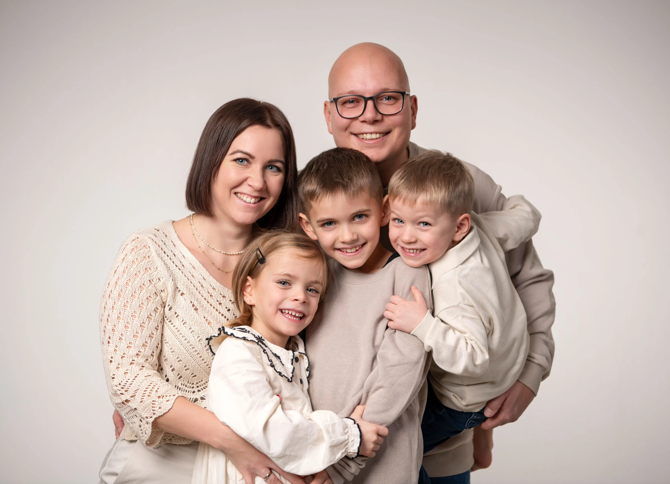 Familie mit drei Kindern umarmt sich eng und lacht in die Kamera