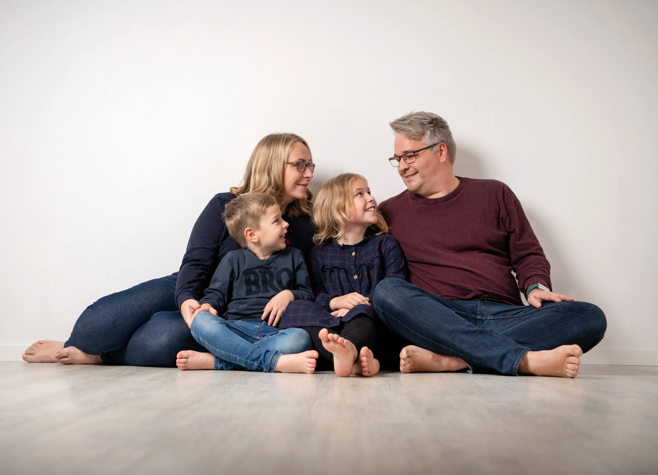 Familienfotos Produktbild 05 | Peter Lauritis Photography Familie mit zwei Kindern in Blau sitzt an eine helle Wand gelehnt auf dem Boden