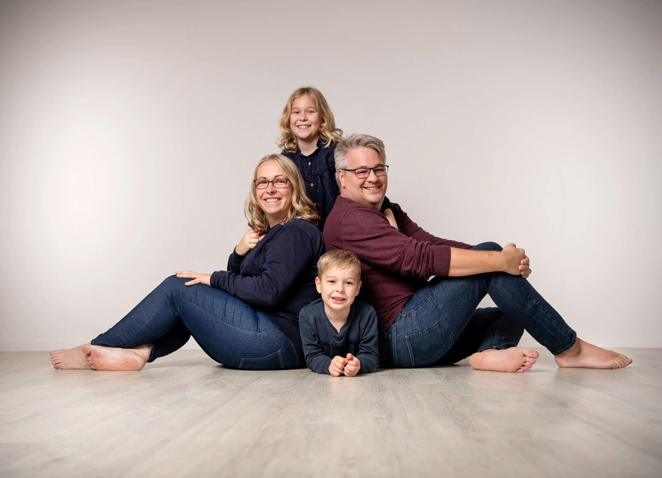 Familienfotos Produktbild 06 | Peter Lauritis Photography Eltern sitzen Rücken an Rücken auf dem Boden, ein Kind steht dahinter, eines liegt davor