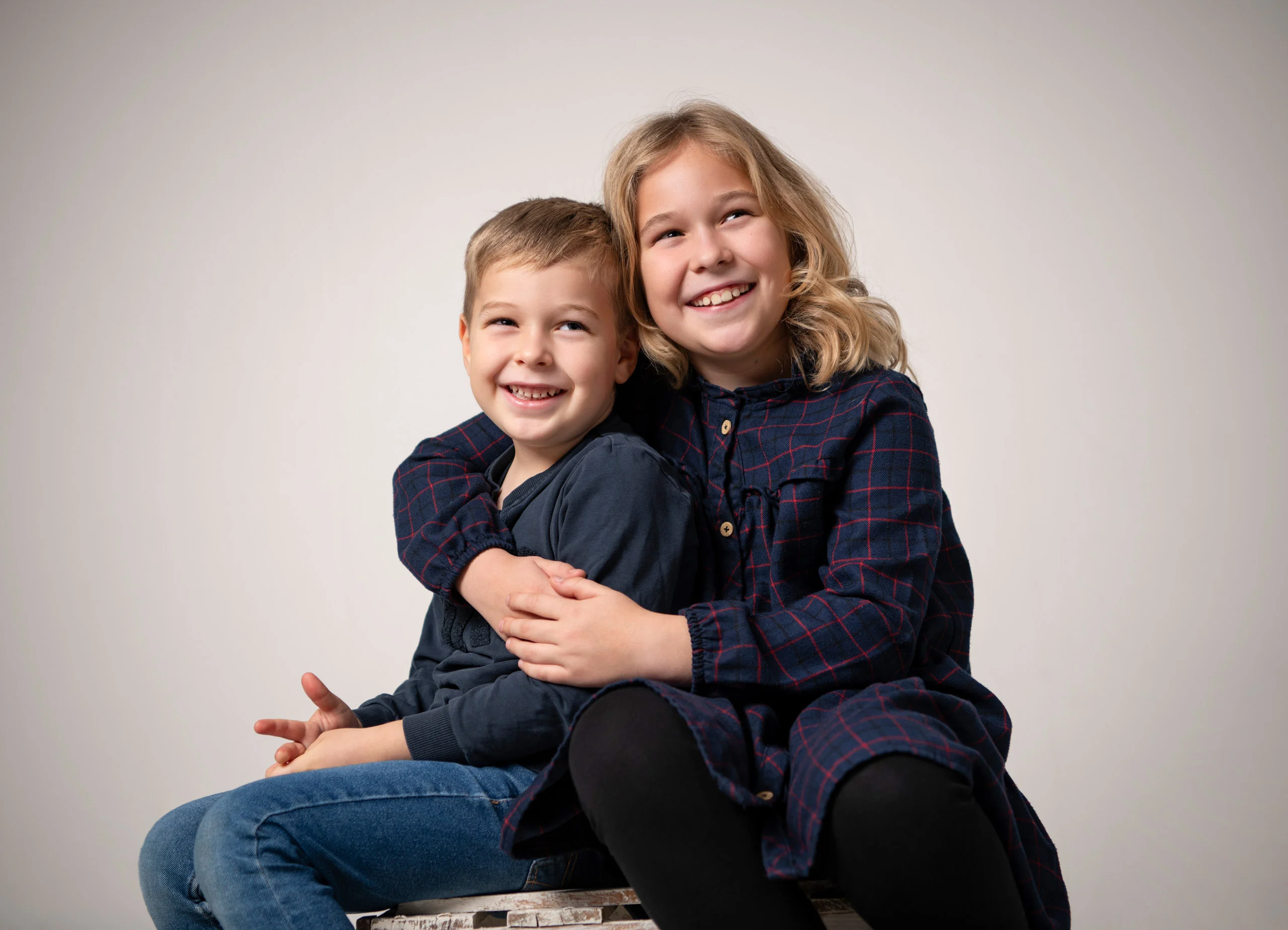 Familienfotos Produktbild 07 | Peter Lauritis Photography Mädchen umarmt lachend ihren kleinen Bruder, beide in dunkelblauer Kleidung