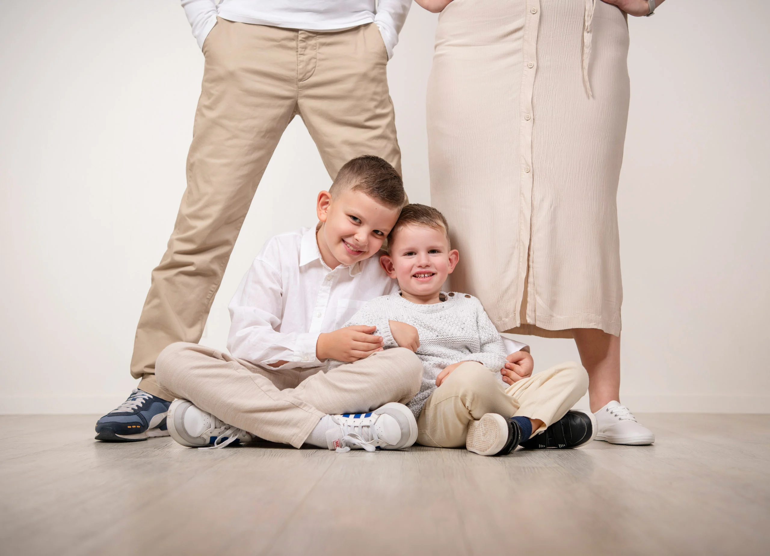 Familienfotos Produktbild 09 | Peter Lauritis Photography Zwei Jungen sitzen auf dem Boden zwischen den Beinen ihrer stehenden Eltern