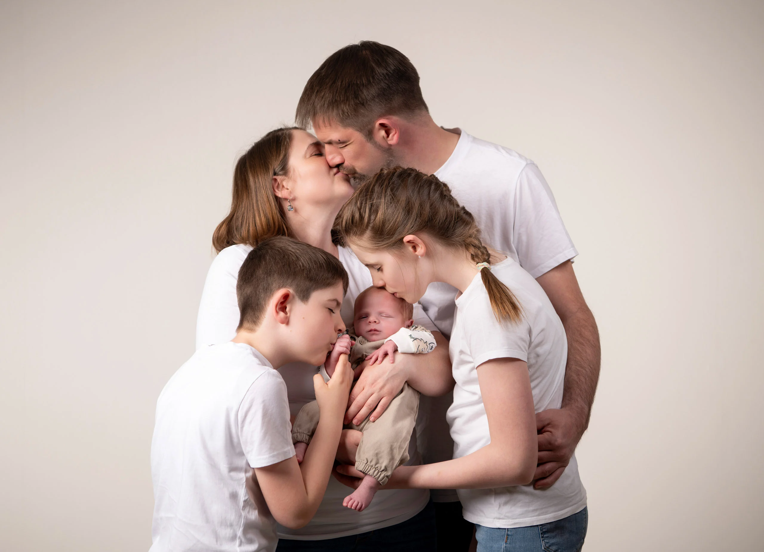 Familienfotos Produktbild 10 | Peter Lauritis Photography Eltern küssen sich, davor küssen zwei Kinder ein Neugeborenes