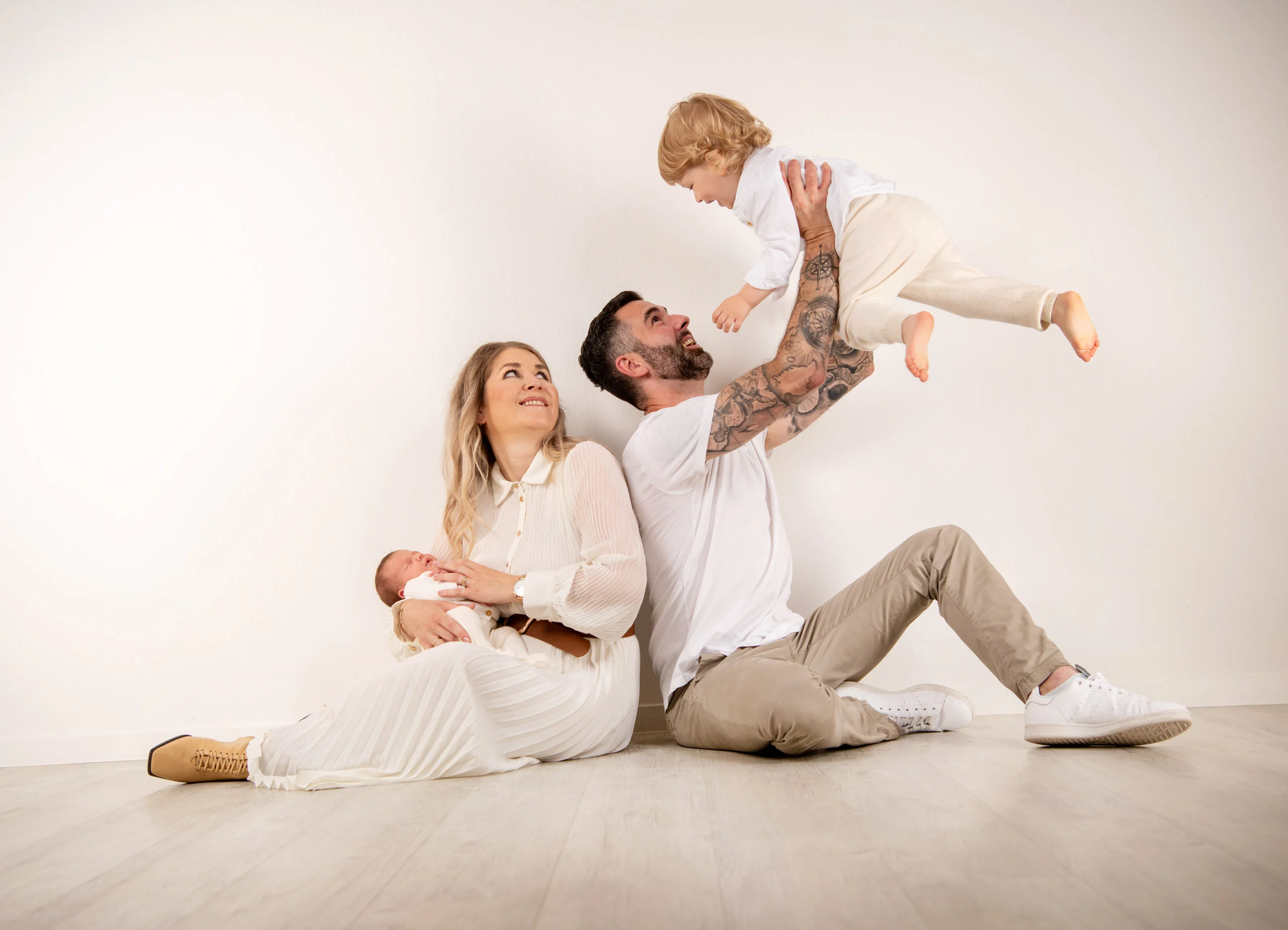 Familienfotos Produktbild 13 | Peter Lauritis Photography Mann wirft ein Kleinkind in die Luft, die Frau sitzt mit einem Baby daneben auf dem Boden